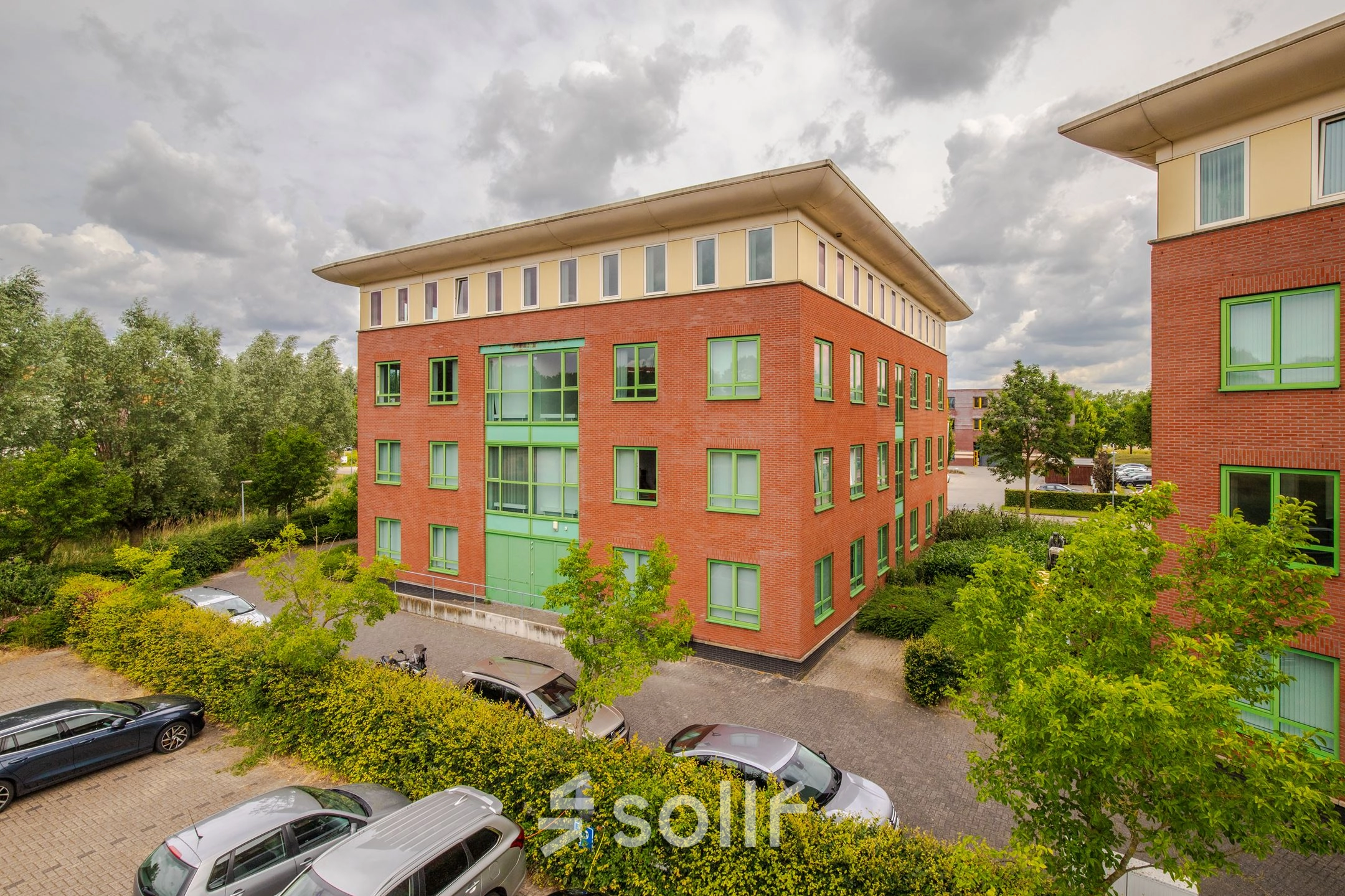 Exterior view of Mercurion 24 in Zevenaar, showcasing the brick and green facade with parked cars in front, ideal for office space rental.