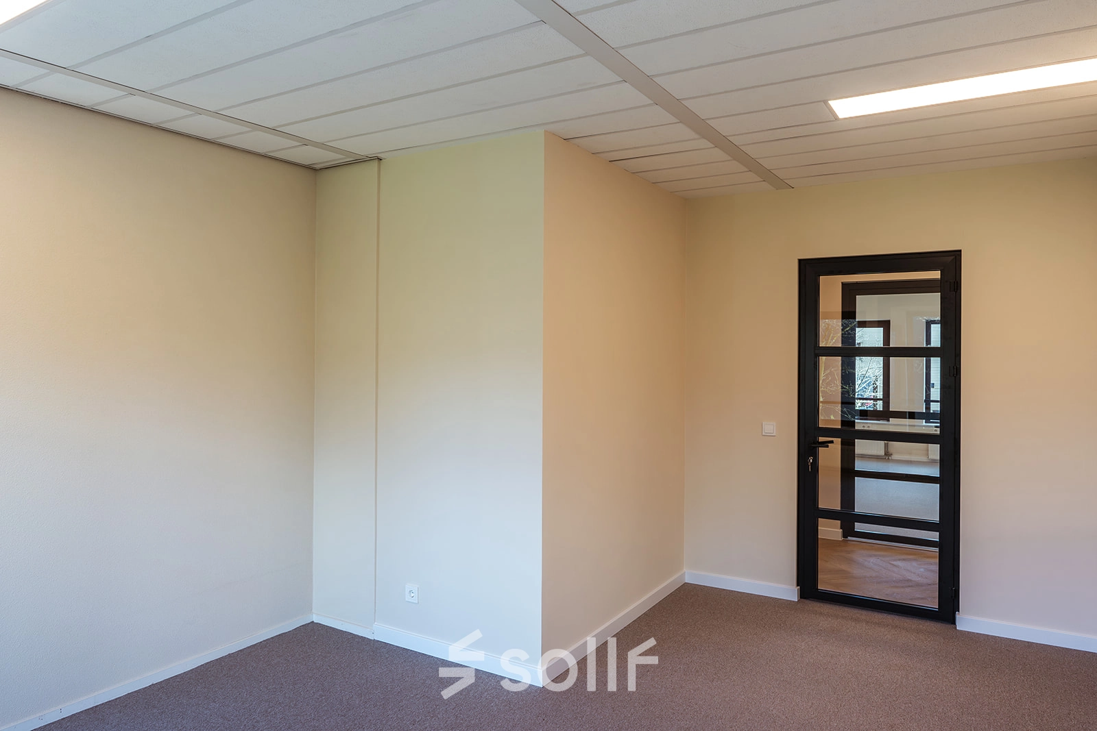 Empty office space with beige walls and carpet, featuring a black-framed glass door at Mercurion 24, Zevenaar, available for office space rental.