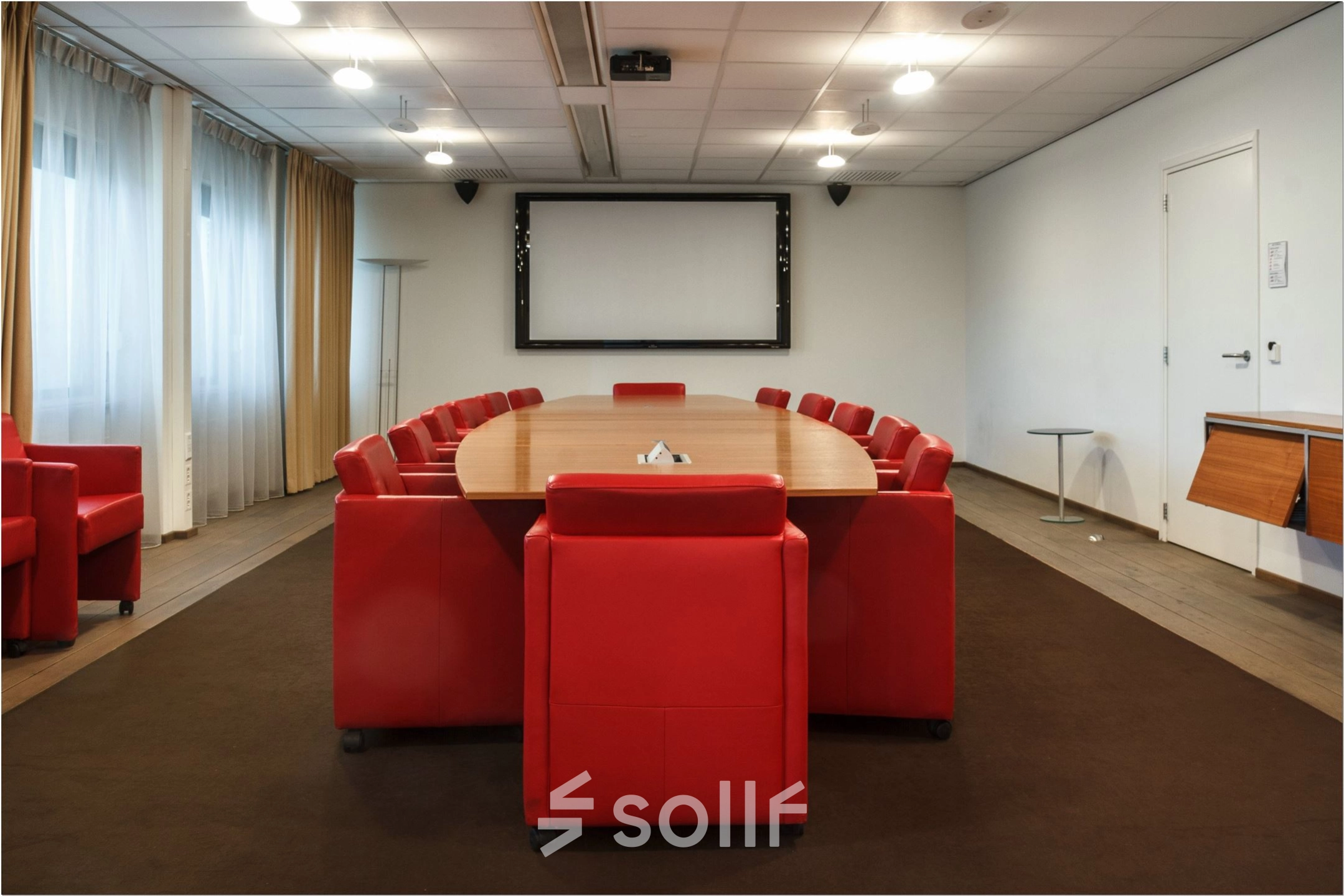 Spacious conference room with a large oval table surrounded by vibrant red chairs, ideal for productive meetings. Located in the office space rental at Bredewater 26, Zoetermeer.