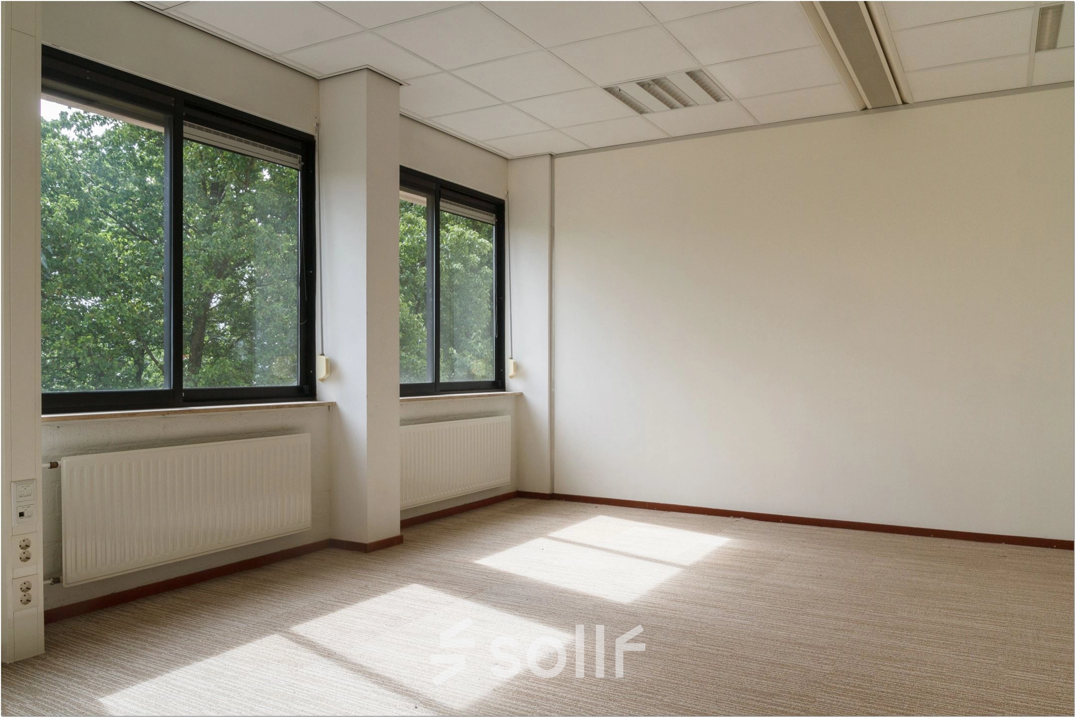 Spacious office with large windows at Bredewater 26, Zoetermeer, offering ample natural light, perfect for an office space rental. The room features a neutral carpet and heating units under the windows.