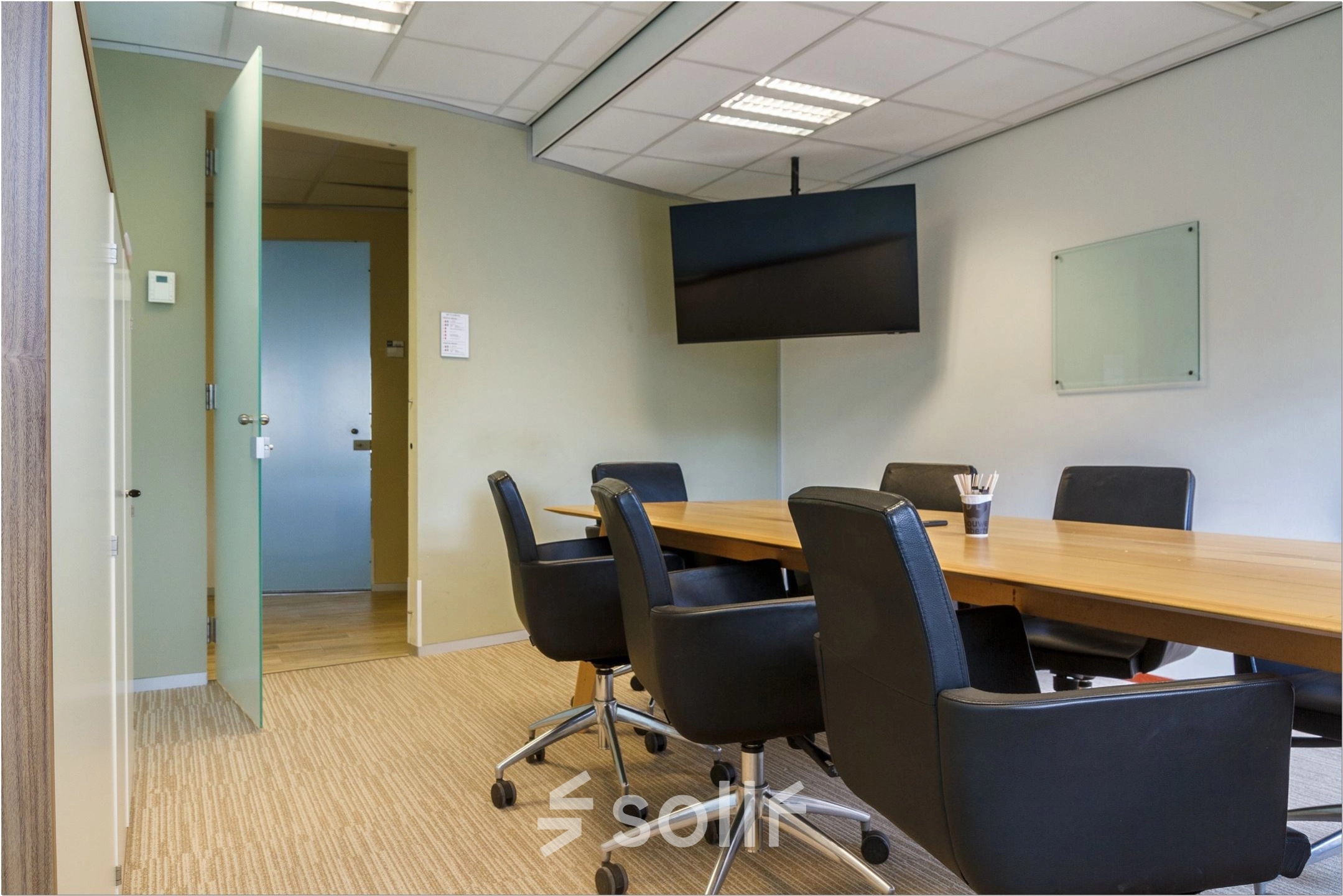 Conference room with a large wooden table, black chairs, and a wall-mounted TV, suitable for office space rental at Bredewater 26, Zoetermeer.