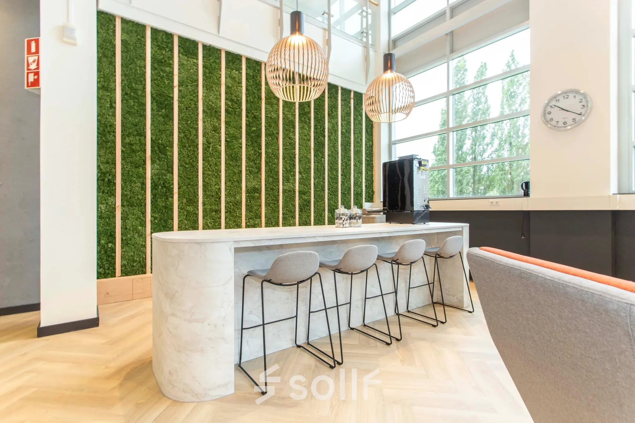 Modern office space available for rent in Zoetermeer, featuring a sleek lounge area with a marble counter, bar stools, and unique lighting fixtures.