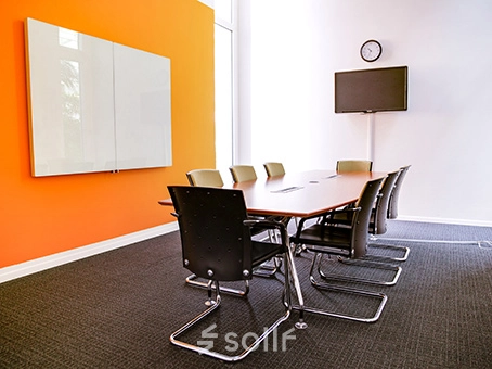 Modern conference room with an orange accent wall and a long table surrounded by chairs, located at Badenerstrasse 47 in Zürich Center. Ideal for office space rental.