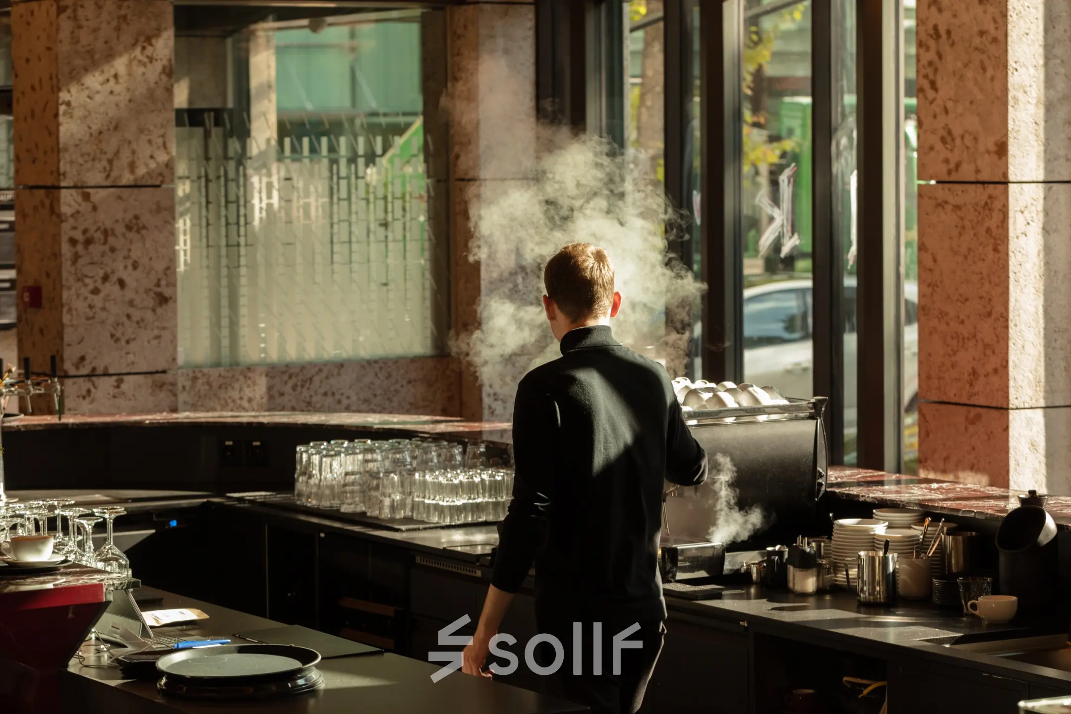 A brightly lit office lounge in Zürich Center at Ernst Nobs Platz 1, featuring a person making coffee. Ideal for those seeking office space rental with amenities.