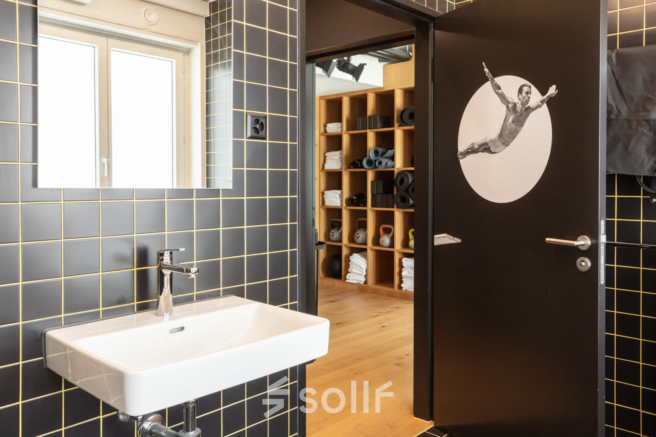 Modern bathroom in office space at Talacker 41, Zürich Center, featuring black tiled walls, a white sink, and shelves in the background.