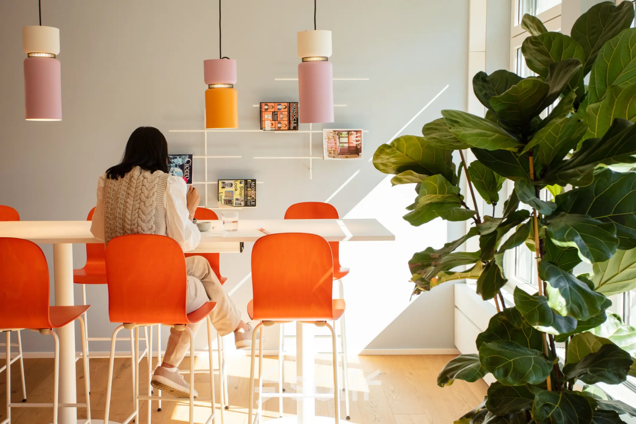Bright office space at Talacker 41, Zürich Center, featuring vibrant orange chairs and a large plant; a person is working at a high table. Ideal for office space rental.