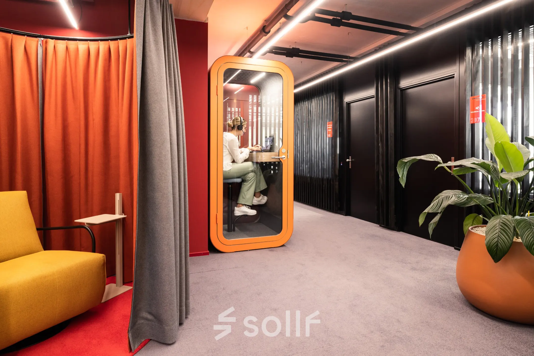Colorful office hallway with a private phone booth, rent office space in Talacker 41, Zürich Center. Decor includes seating and large plant.