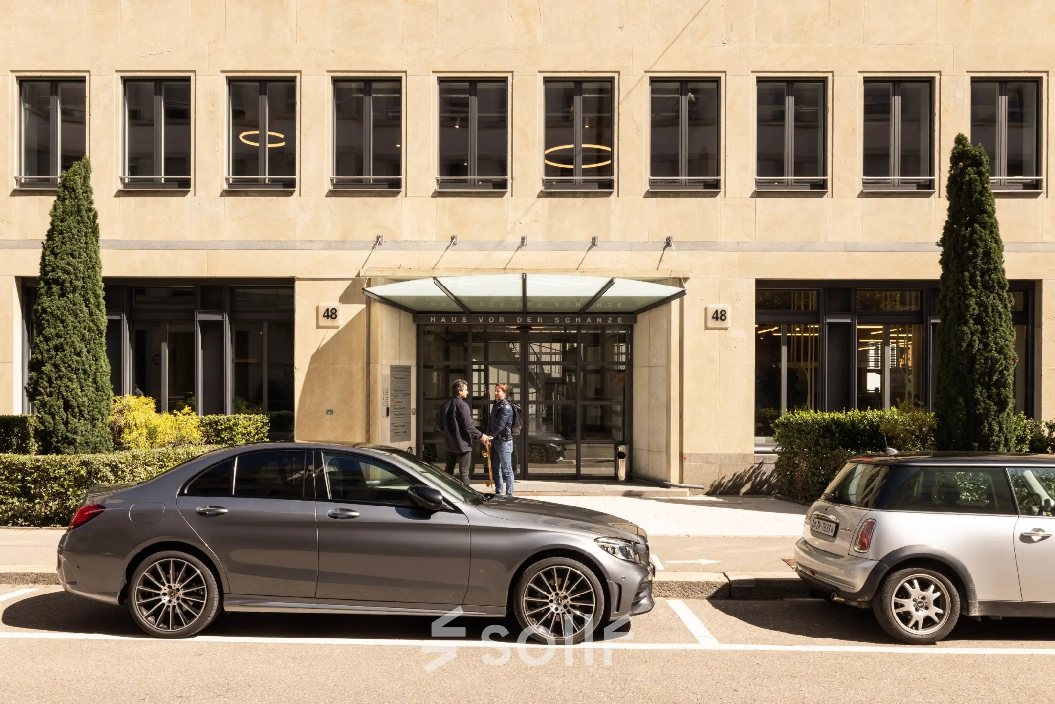 Exterior of an office building at Beethovenstrasse 48, Zürich Enge, featuring two people conversing near the entrance, ideal for office space rental.