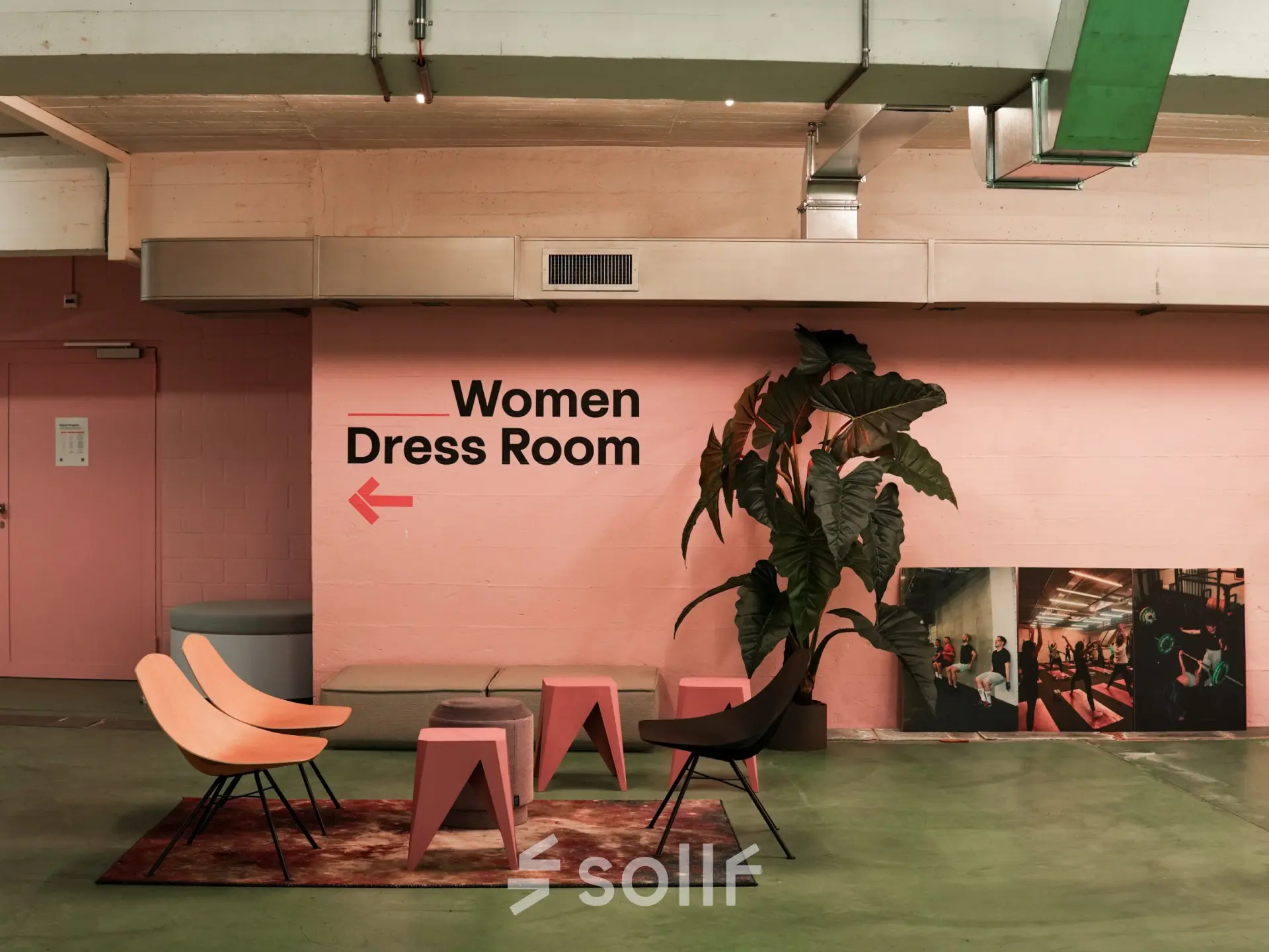 A modern office space with colorful seating, green flooring, and pink walls featuring a sign for a Women's Dress Room, ideal for office space rental.