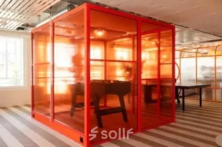 Bright office space rental at Stockerstrasse 33, Zürich Enge, featuring a vibrant red glass meeting pod and striped flooring.