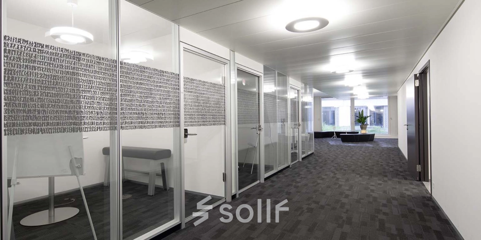 Modern office space for rent at Europaallee 41 in Zürich Mitte, featuring glass-walled meeting rooms and a well-lit hallway.