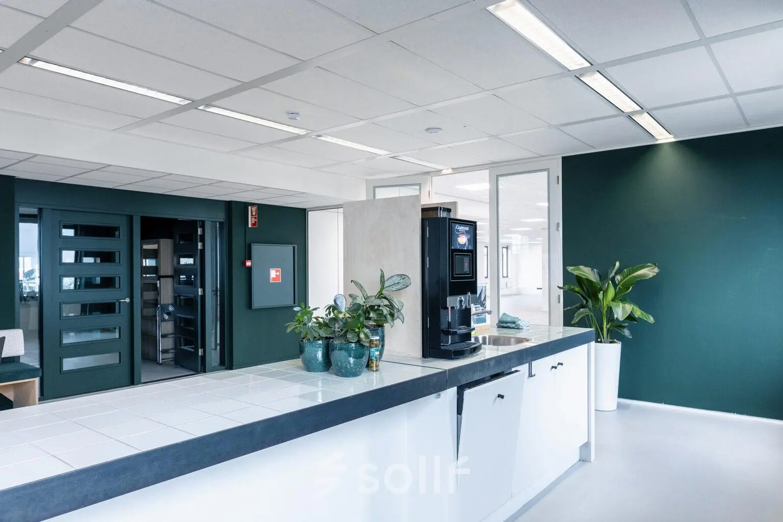 Modern office space with a kitchenette featuring a coffee machine and plants at Hanzeplein 11-27, Zwolle, perfect for office space rental or an office to rent.