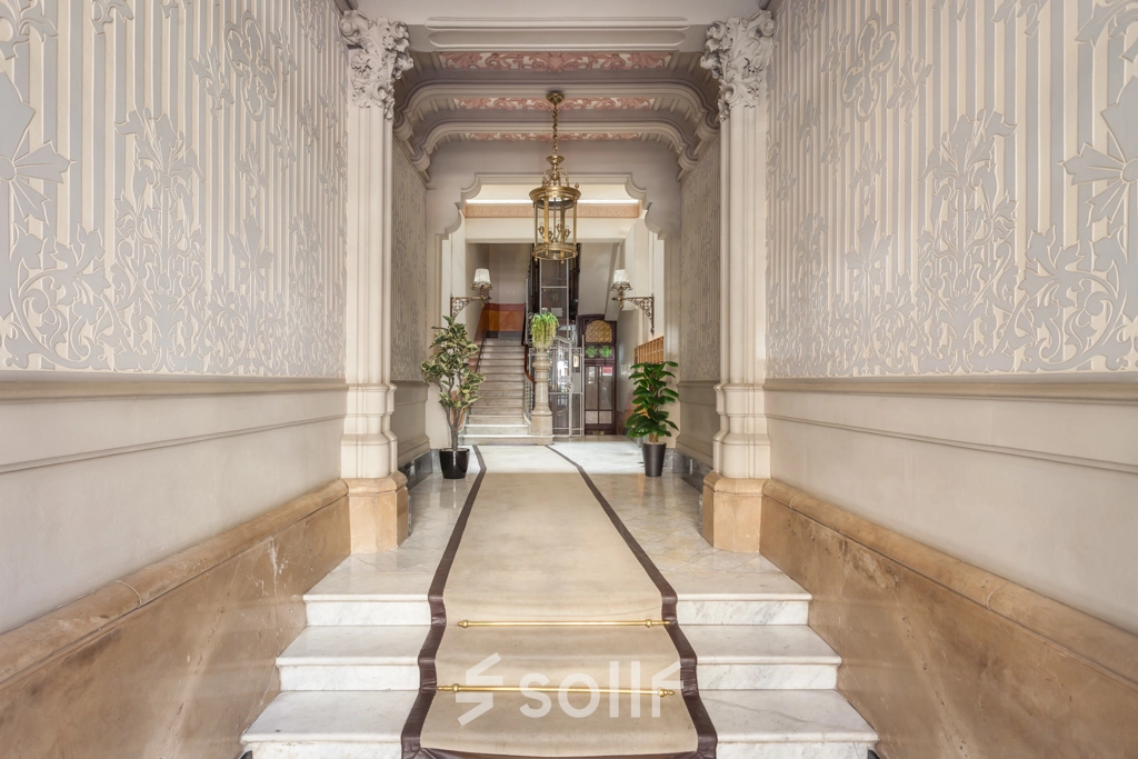 Entrada elegante y señorial para alquilar una oficina en Barcelona Eixample, Rambla de Catalunya 125, con suelo de mármol y detalles ornamentales en las paredes.