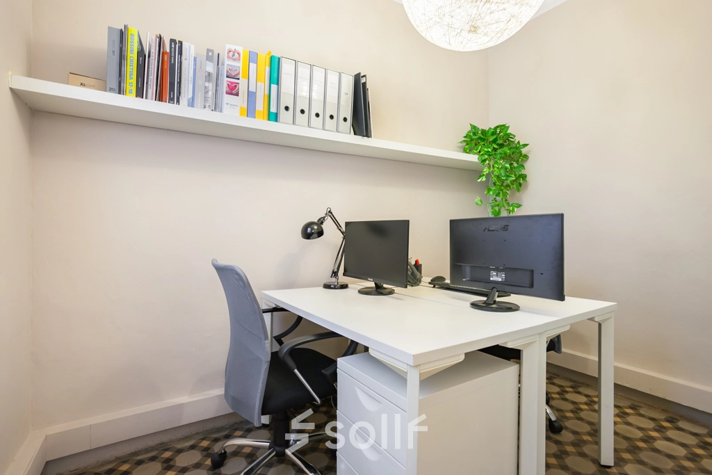 Espacio de trabajo luminoso ideal para alquilar una oficina en Rambla de Catalunya 125, Barcelona Eixample, con escritorio ordenado, silla ergonómica y estantería con documentos.