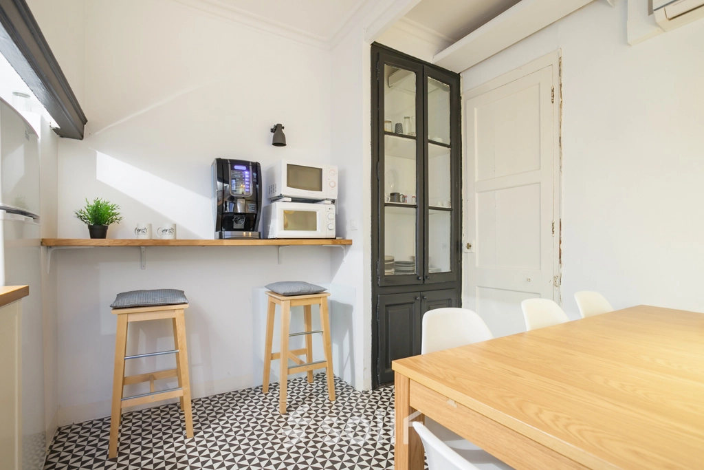 Espaciosa área de descanso en alquiler de oficinas en Barcelona Eixample, con mesas de madera y zona de café, iluminación natural y decoración moderna.
