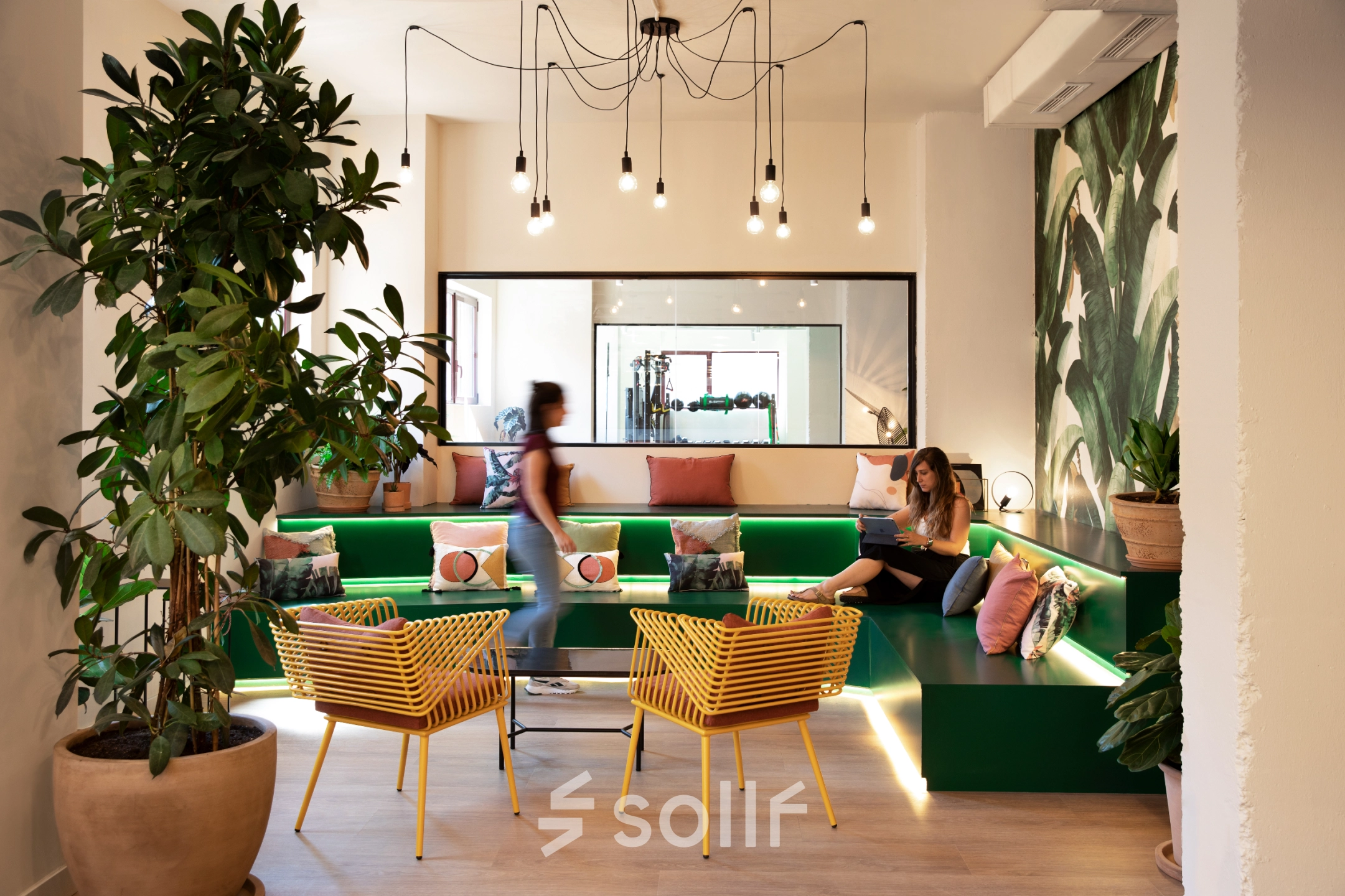 Luminosa sala de espera en alquiler de oficinas en Paseo Imperial 14, Madrid Centro, con sofás verdes, sillas amarillas y decoración moderna.