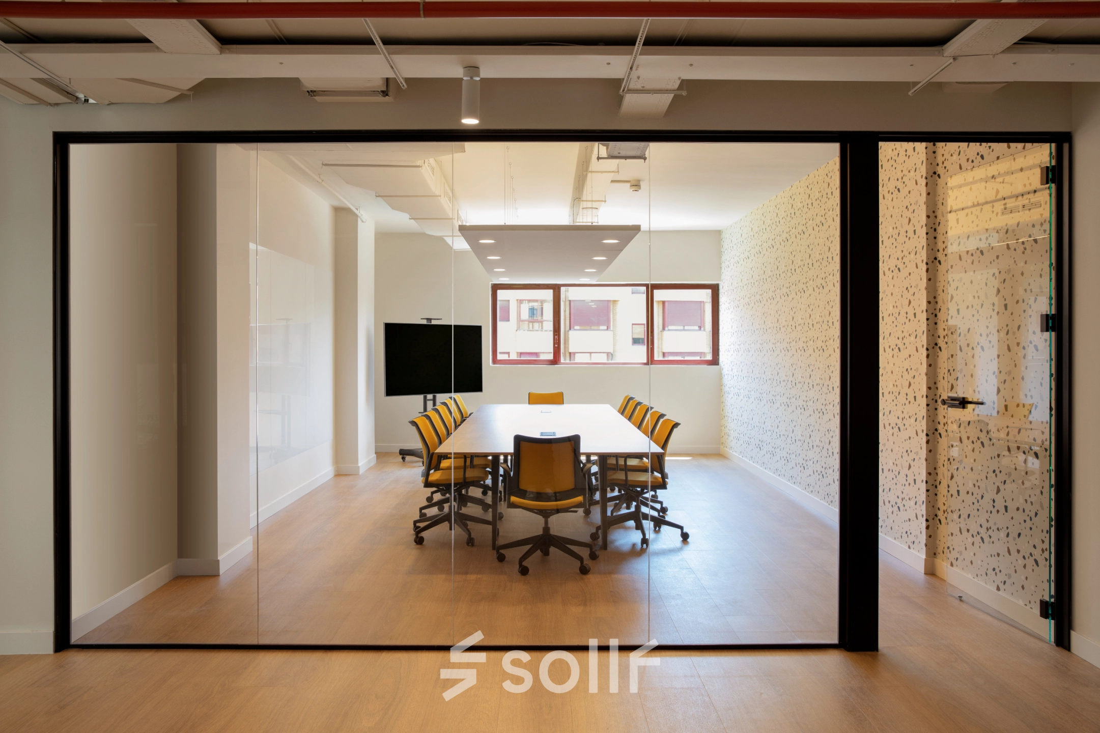Sala de reuniones moderna para alquilar una oficina en Paseo Imperial 14, Madrid Centro, con mesa grande, sillas amarillas y pantallas digitales.