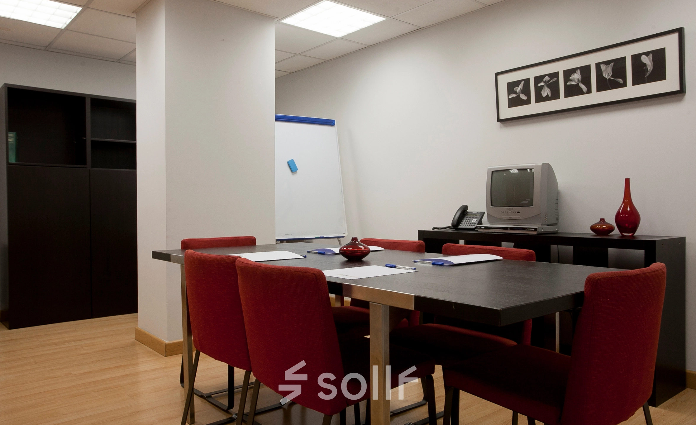 Oficina en alquiler ubicada en Calle Lagasca 95, Madrid Salamanca, equipada con mesa de reuniones, sillas rojas y un mueble con televisión.