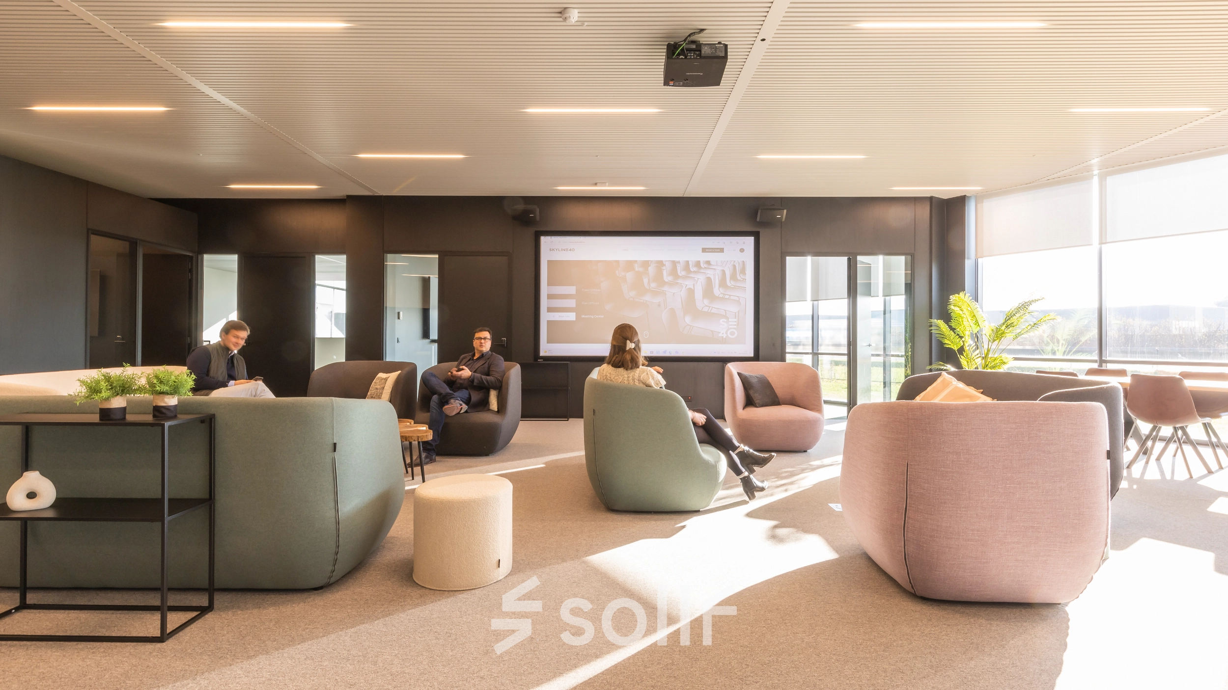 Moderne kantoorruimte op Korte Keppestraat 19 in Aalst met comfortabele zitmeubels en een groot presentatiescherm. Mensen zijn bezig met werkbesprekingen in deze lichte en uitnodigende omgeving.