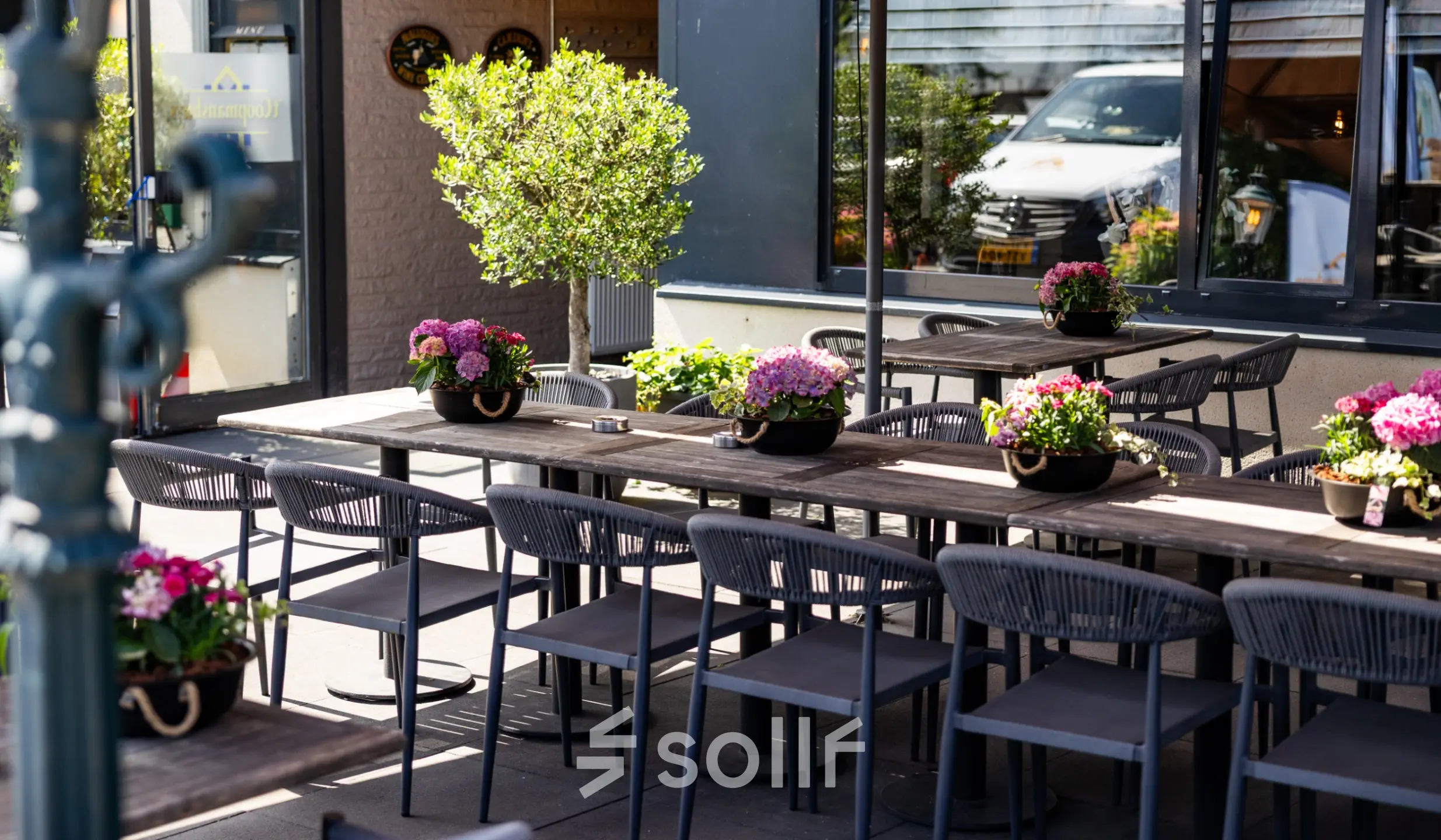 Terras aan Bedrijvenpark Twente 305 in Almelo met houten tafels, stoelen en planten, geschikt voor ontspannen vergaderingen of pauzes.