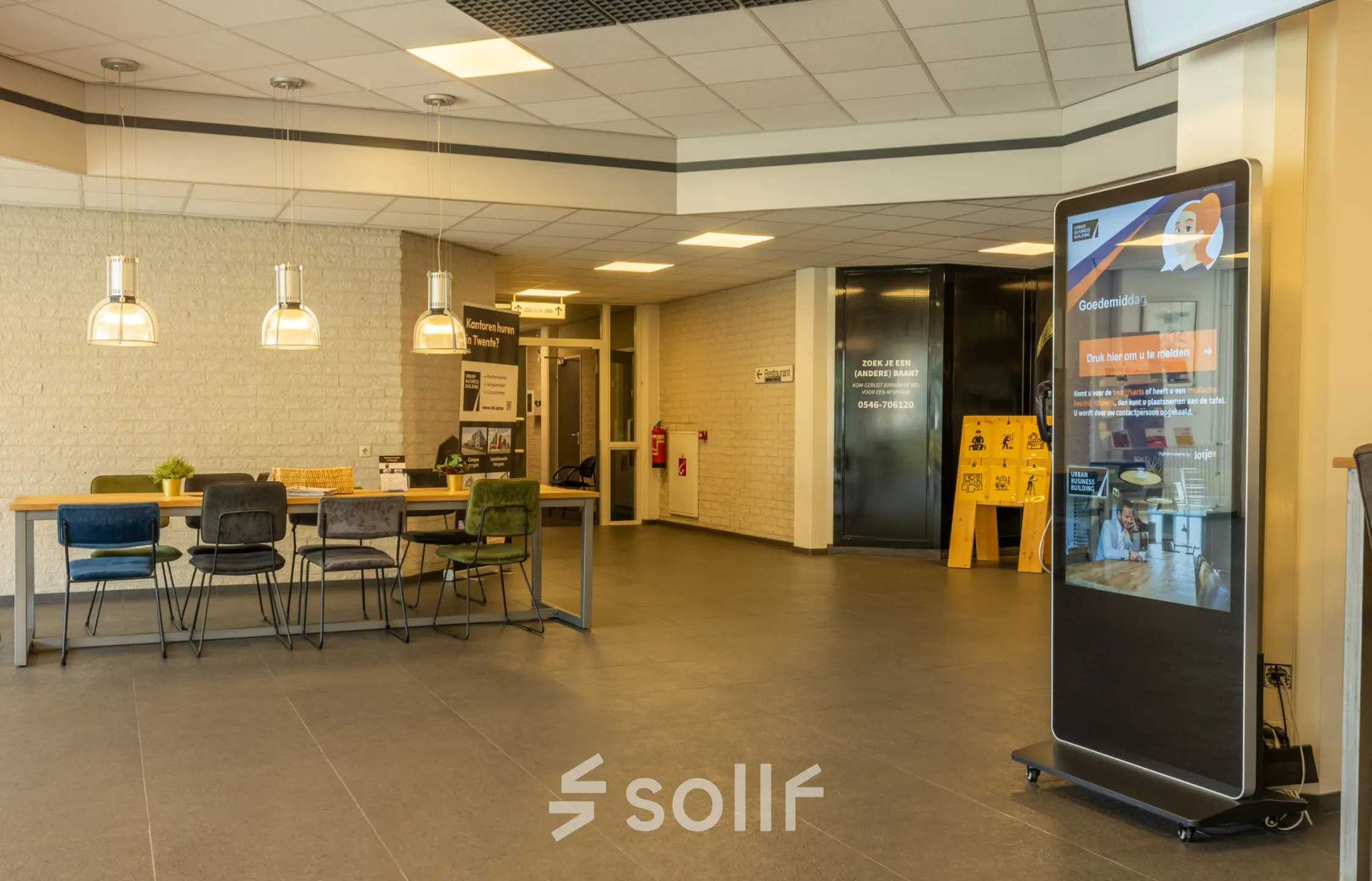 Ruime entree van een kantoorpand op Bedrijvenpark Twente 305, Almelo, met moderne meubels en een informatiescherm. Ideaal voor wie kantoorruimte wil huren in een inspirerende omgeving.