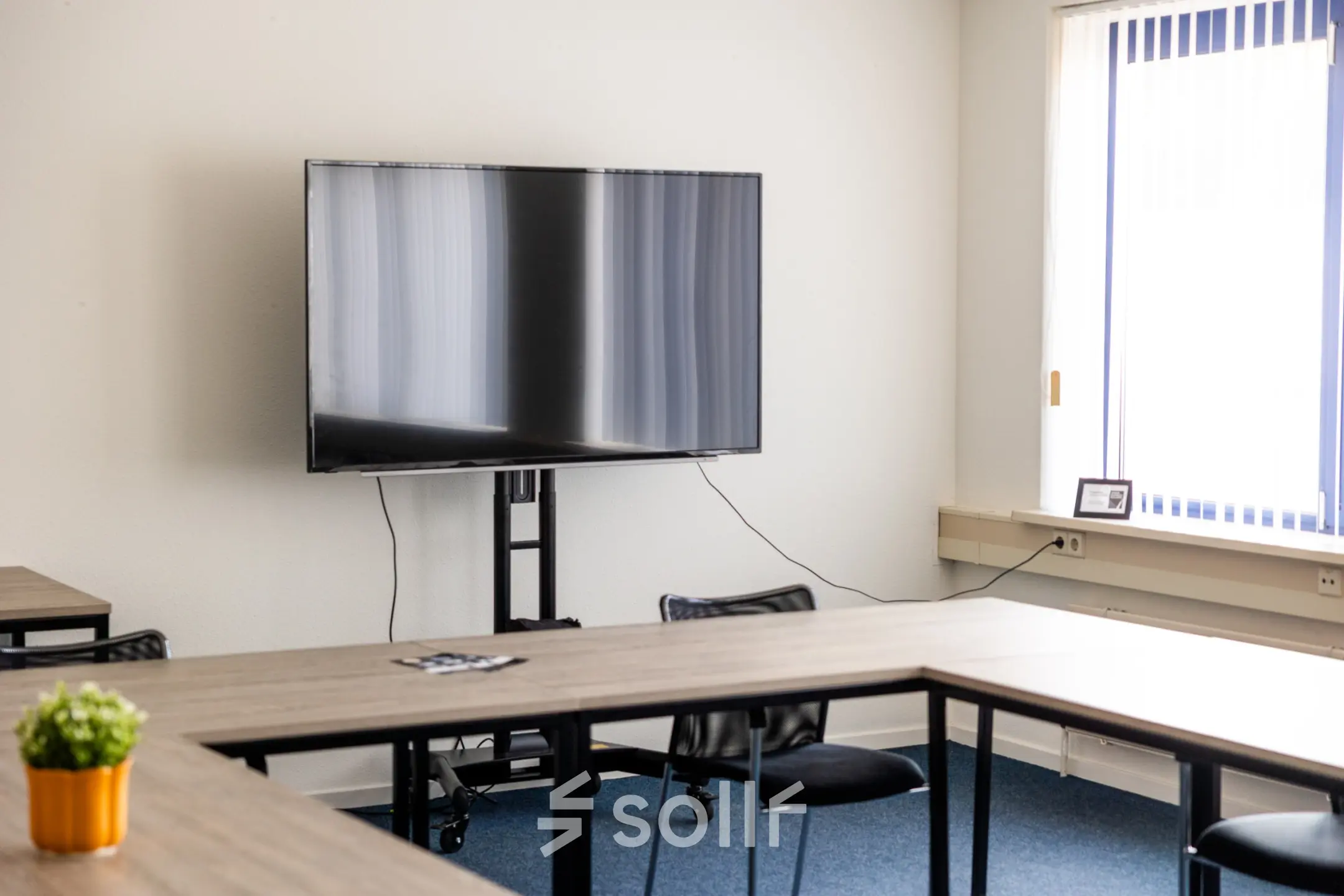 Kantoorruimte te huur op Bedrijvenpark Twente 305 in Almelo, met houten tafels, een grote televisie aan de muur en veel natuurlijk licht door het raam.