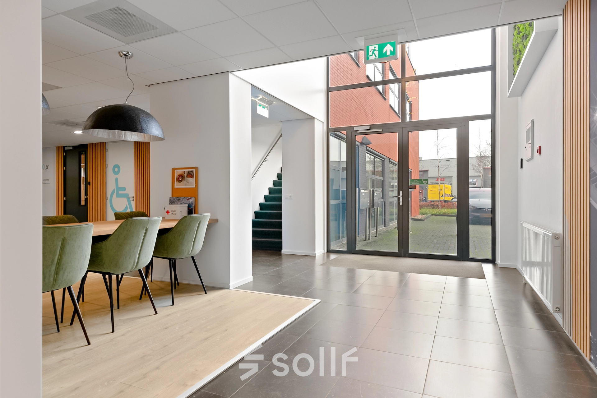 In de lichte entree van het kantoorpand aan de Jool Hulstraat 2-14 in Almere Stad staan groene stoelen bij een houten tafel. De kantoorruimte is geschikt om te huren.