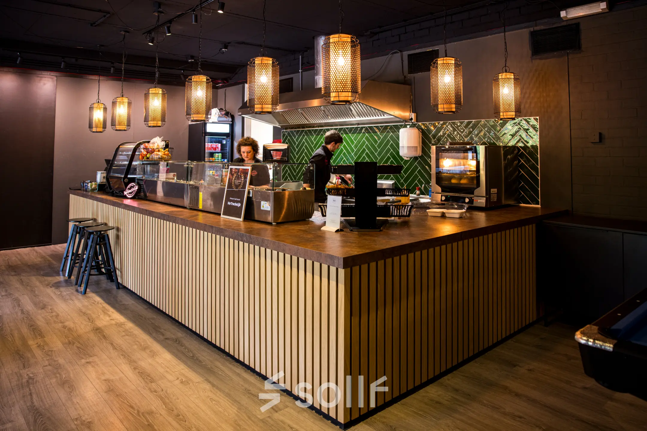 Sfeervolle kantoorruimte huren op Markerkant 1310 in Almere Stad, met een uitnodigende lounge sfeer en houten elementen. Twee mensen zijn bezig met bereiden van drankjes aan de bar.