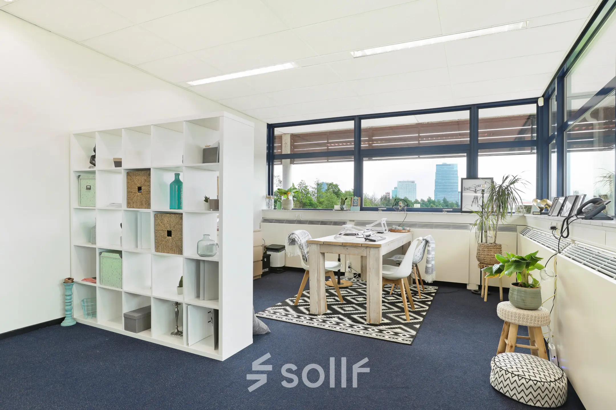 Lichte kantoorruimte met grote ramen en zicht op Almere Stad, voorzien van vergadertafel en decoratieve elementen. Geschikt voor werkruimte of vergaderruimte voor wie kantoorruimte wil huren.