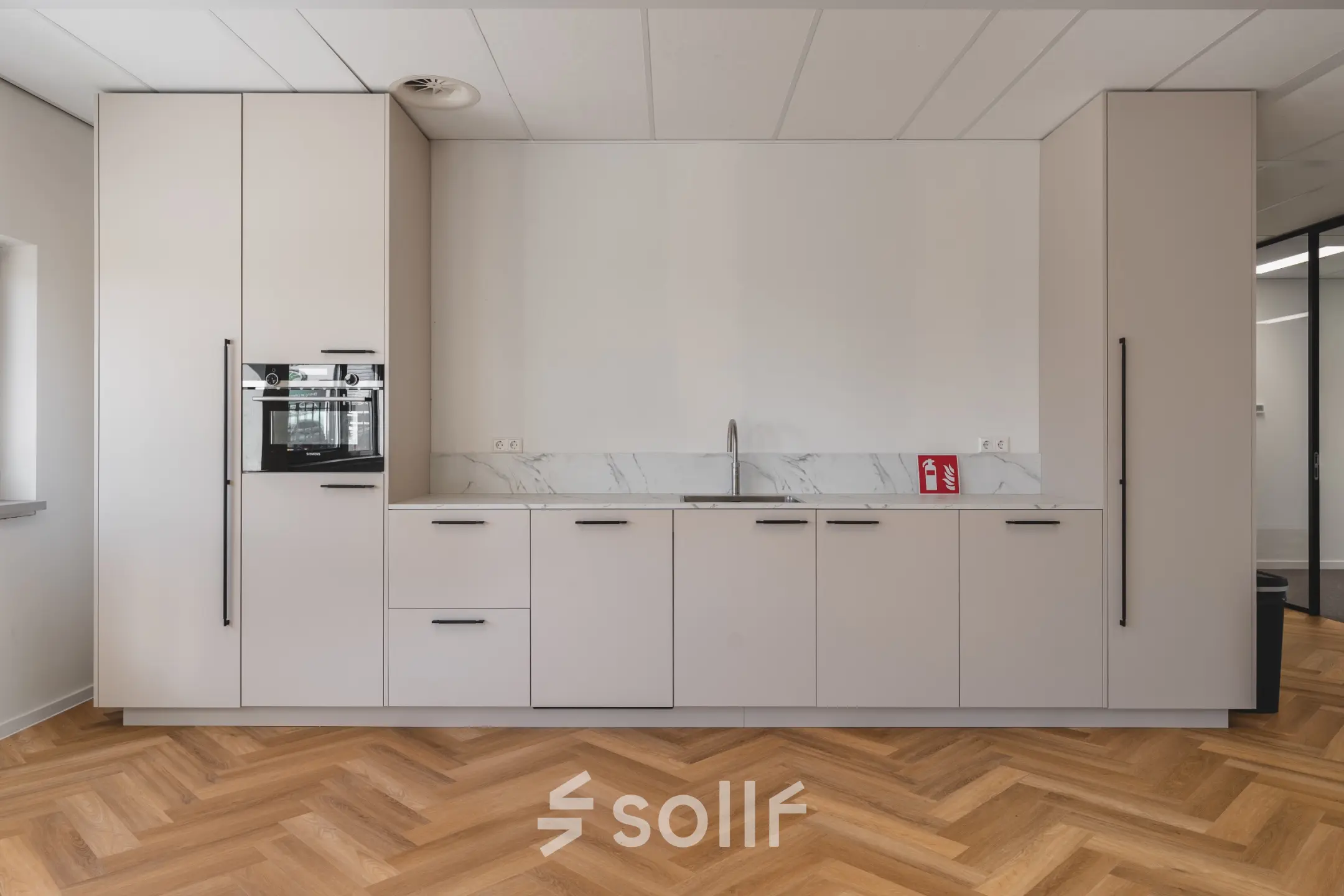 Heldere kantoorruimte in Almere Stad met moderne keuken, ideaal voor kantoorruimte huren. Strakke opstelling met houtpatroon vloer, witte kasten en ingebouwde apparatuur.
