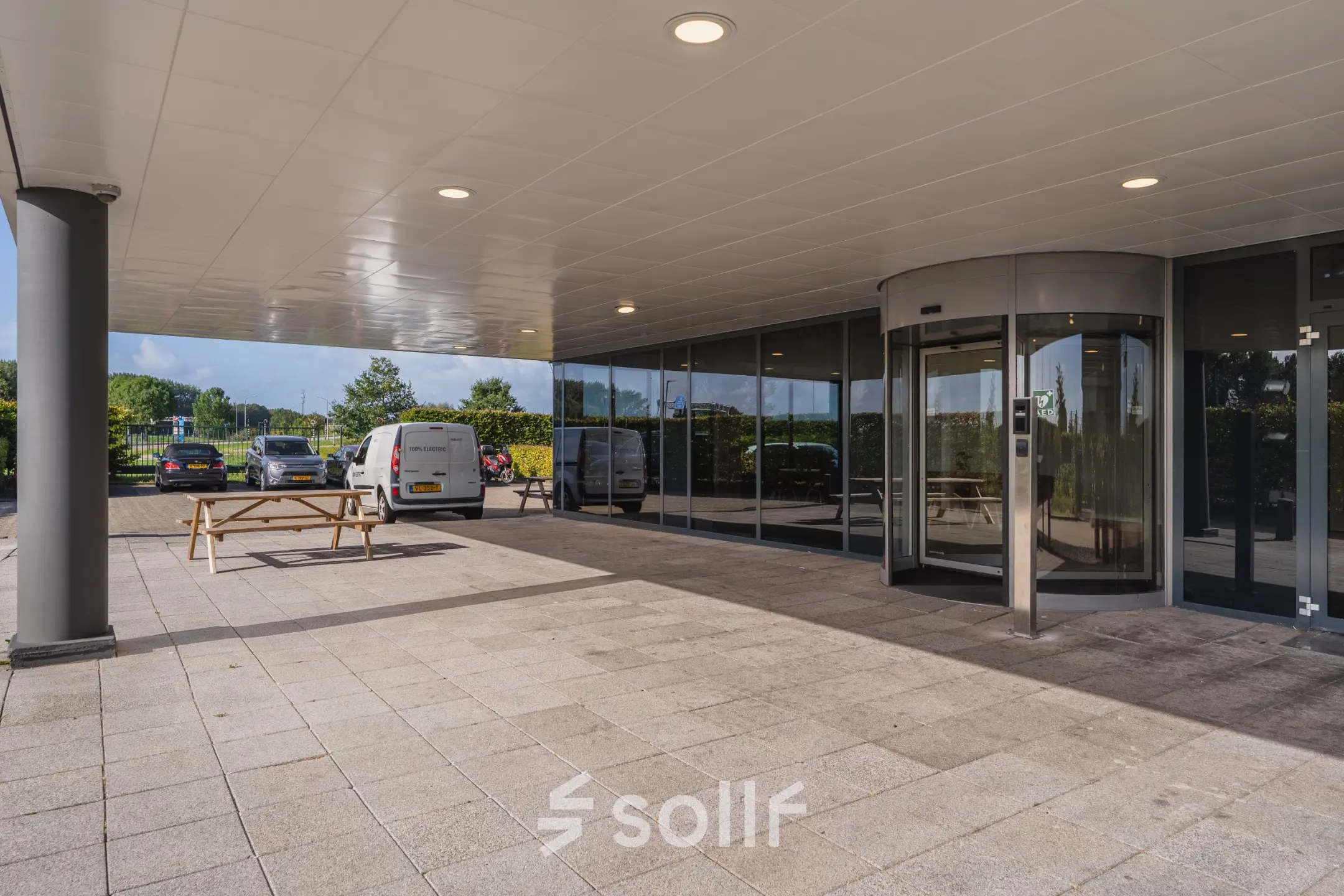 Entree van Veluwezoom 15 in Almere Stad met een draaideur en zitgelegenheid buiten. Ideaal voor bedrijven die op zoek zijn naar kantoorruimte om te huren.