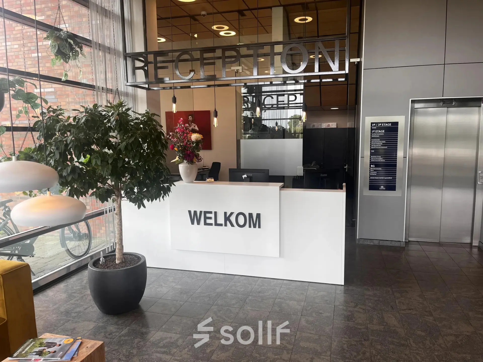 Moderne receptie in een kantoorpand op Leidse Schouw 2, Alphen aan den Rijn, met een balie, planten en kunst. Ideaal voor wie kantoorruimte wil huren.