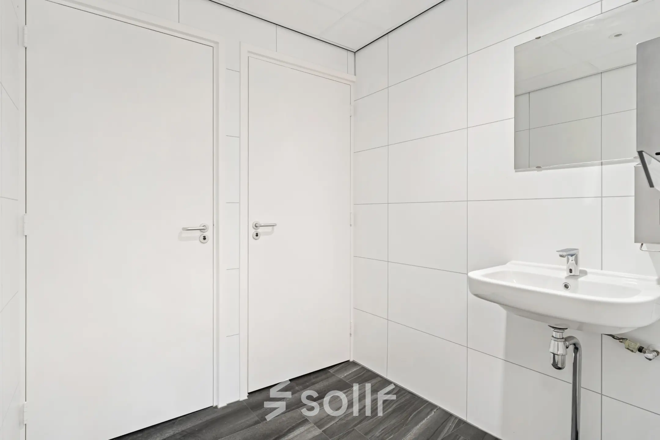 Wit betegelde toiletruimte in kantoorpand met wastafel en spiegel op Maanlander 43, Amersfoort Calveen. Kantoorruimte huren in een nette omgeving.