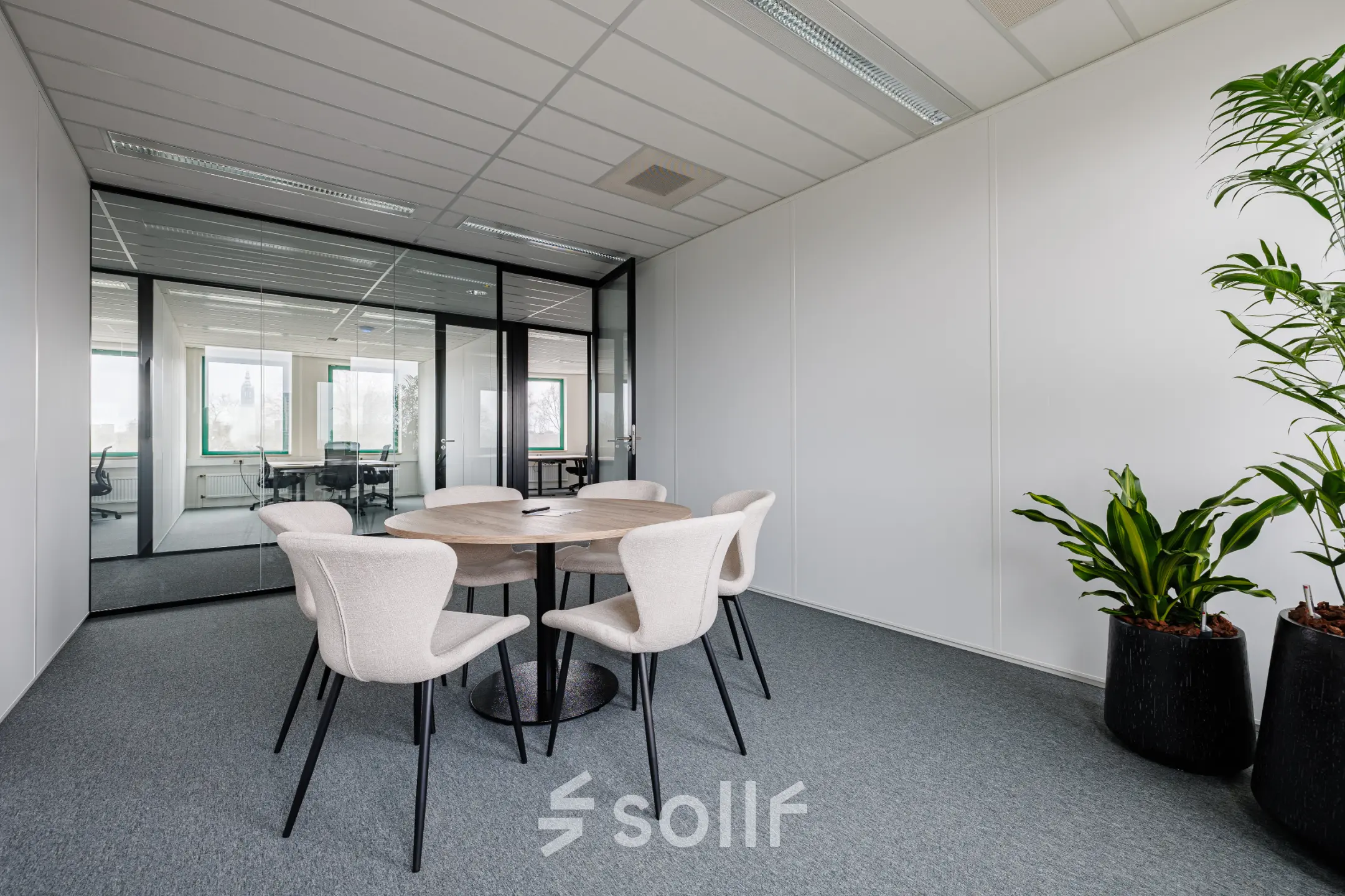Moderne kantoorruimte huren op Stadsring 201, Amersfoort Centrum. Ruimte met een ronde tafel en vijf stoelen, natuurlijke lichtinval en planten in de hoeken van het kantoorpand.