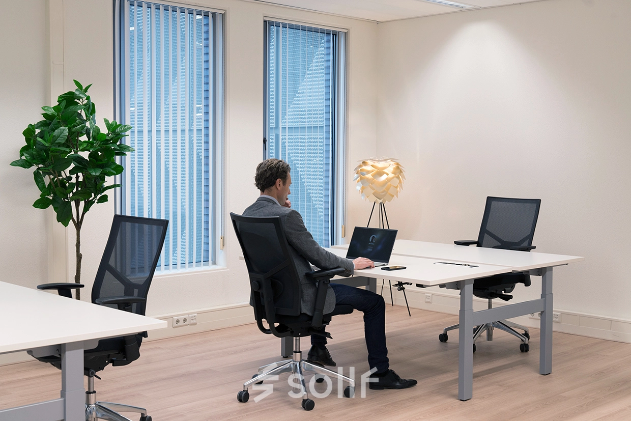 Kantoor aan de Handelsweg 53 in Amstelveen met een man die aan een bureau werkt op een laptop. Lichte, ruime werkplekken met moderne stoelen en groene planten.