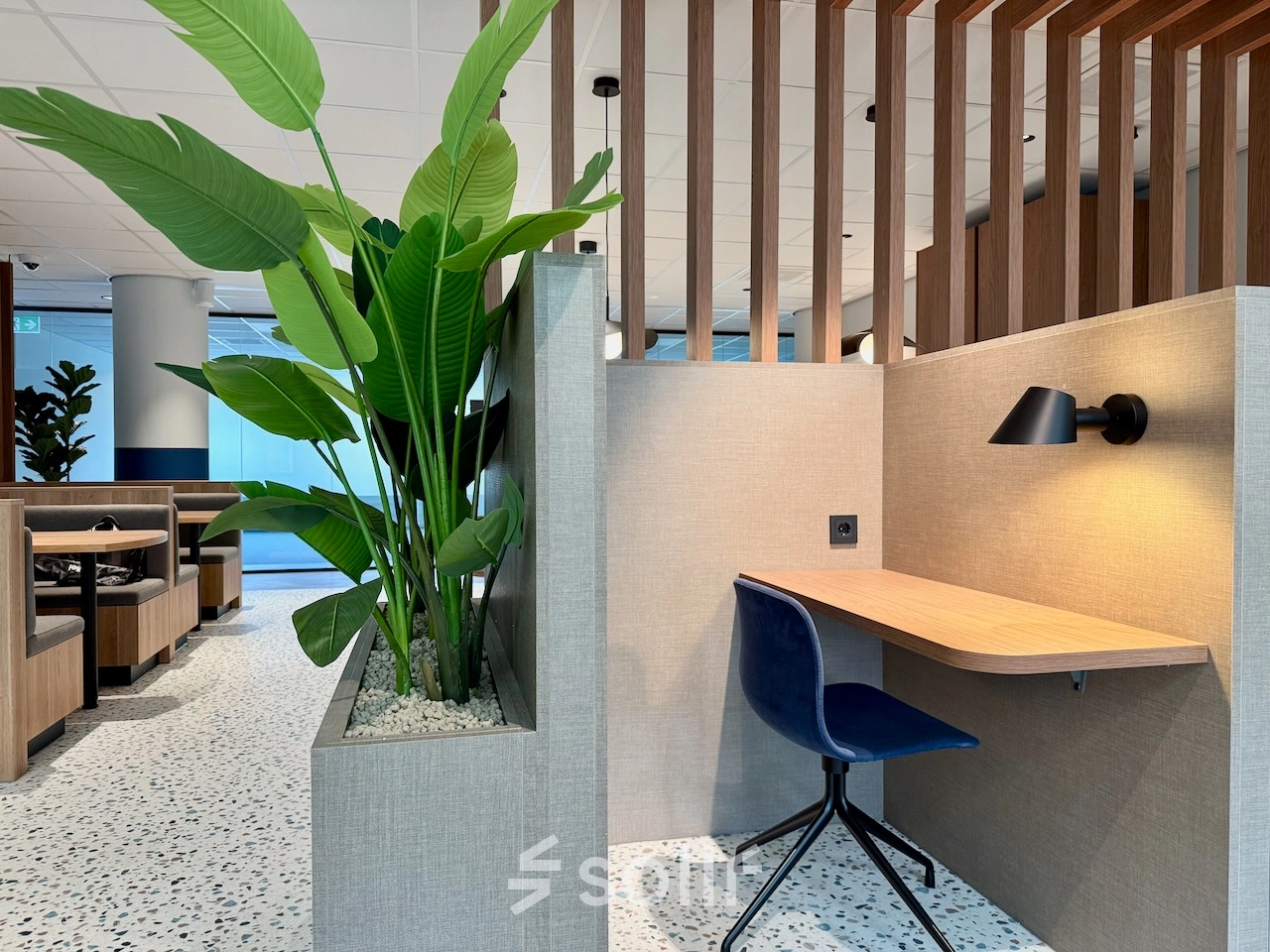 Moderne kantoorruimte met houten scheidingswanden, groene planten en een werkplek met een blauwe stoel. Ideaal om als kantoor te huren in Amstelveen, aan de Professor E.M. Meijerslaan 1.