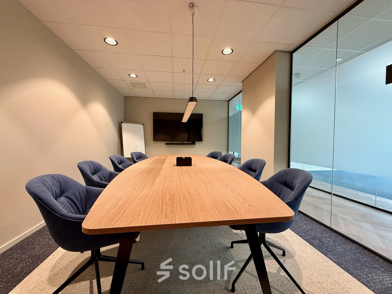 Kantoorruimte huren in Amstelveen: moderne vergaderruimte met comfortabele stoelen, houten tafel, en een flatscreen aan de muur.