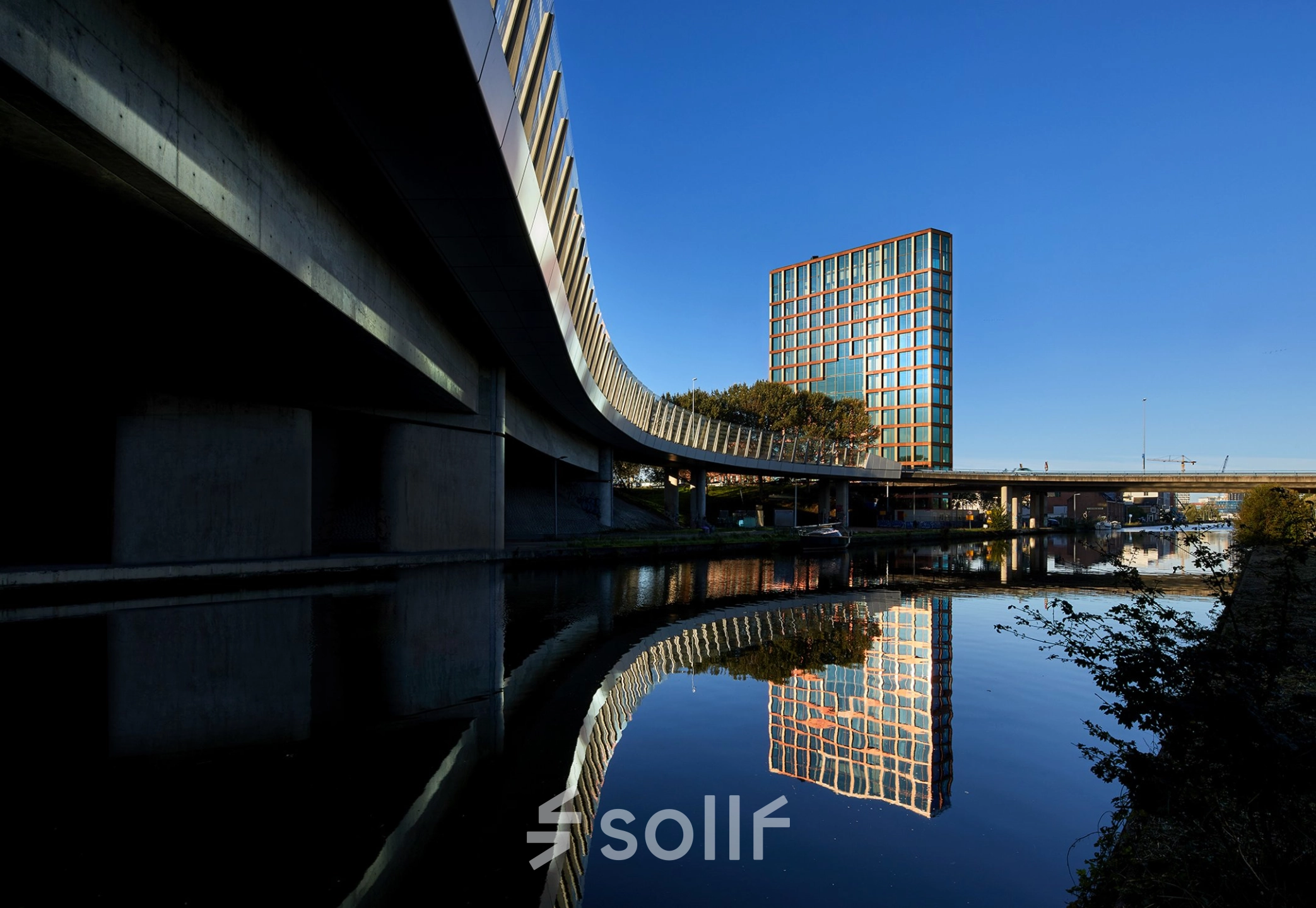 Moderne buitenkant van het kantoorpand aan H.J.E. Wenckebachweg 230-258, gelegen in Amsterdam Amstel Business Park, met reflecties in het water. Perfecte locatie voor kantoorruimte huren.