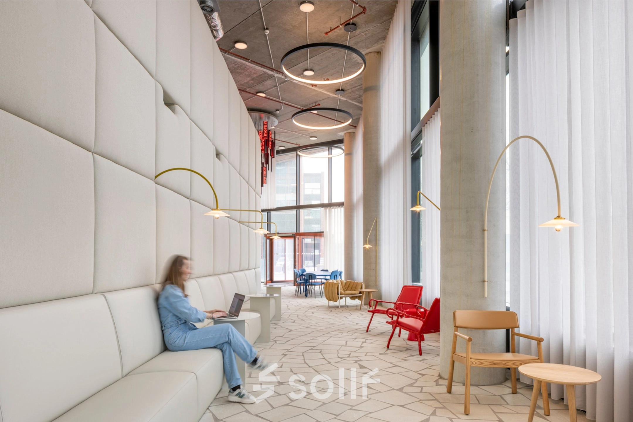 Lichte en moderne lounge in een kantoorpand aan H.J.E. Wenckebachweg 230-258, Amsterdam met gedempte verlichting en stijlvolle zitbanken. Een persoon werkt op een laptop, wat de zakelijke sfeer benadrukt.