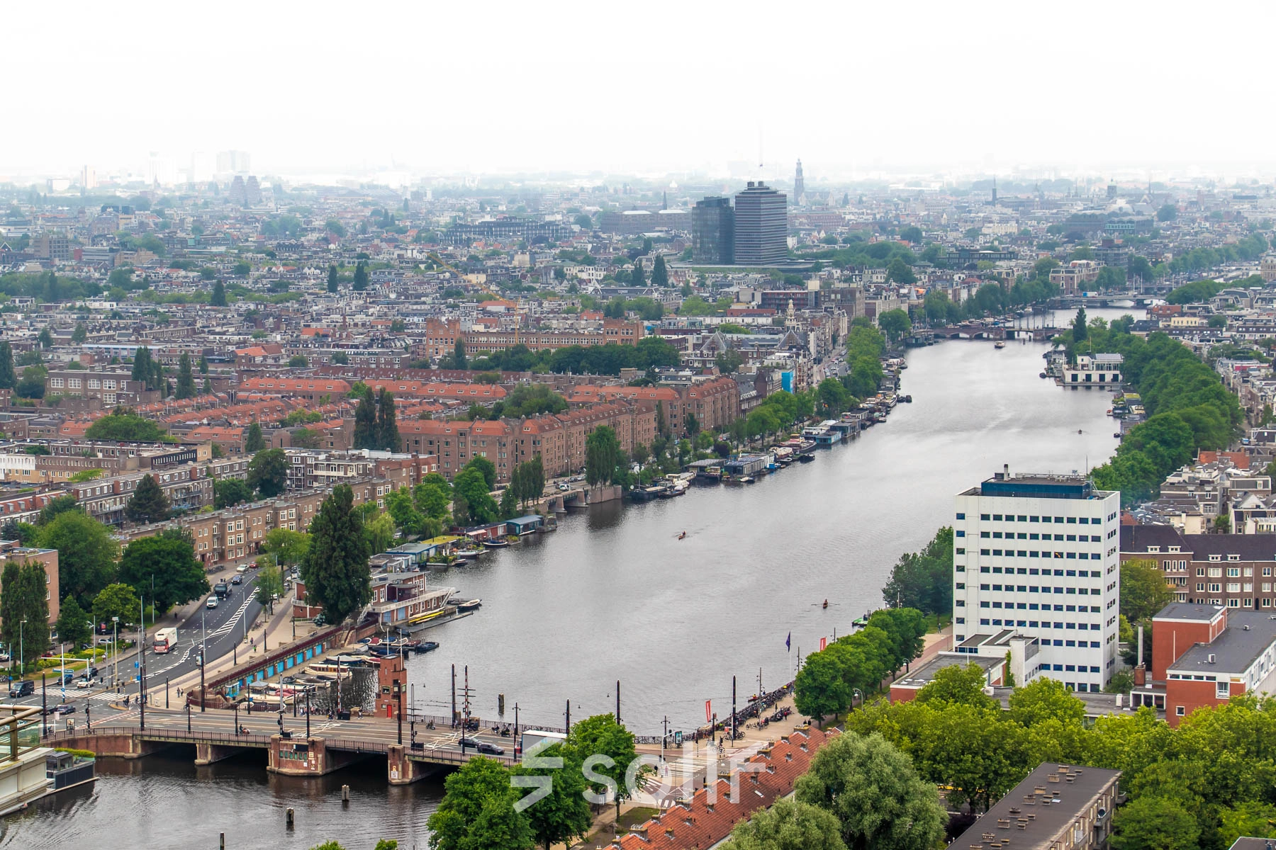 Uitzicht op Amstelplein 8 in Amsterdam Amstel, met de rivier en de stad op de achtergrond. Een kantoorpand is zichtbaar nabij het water.