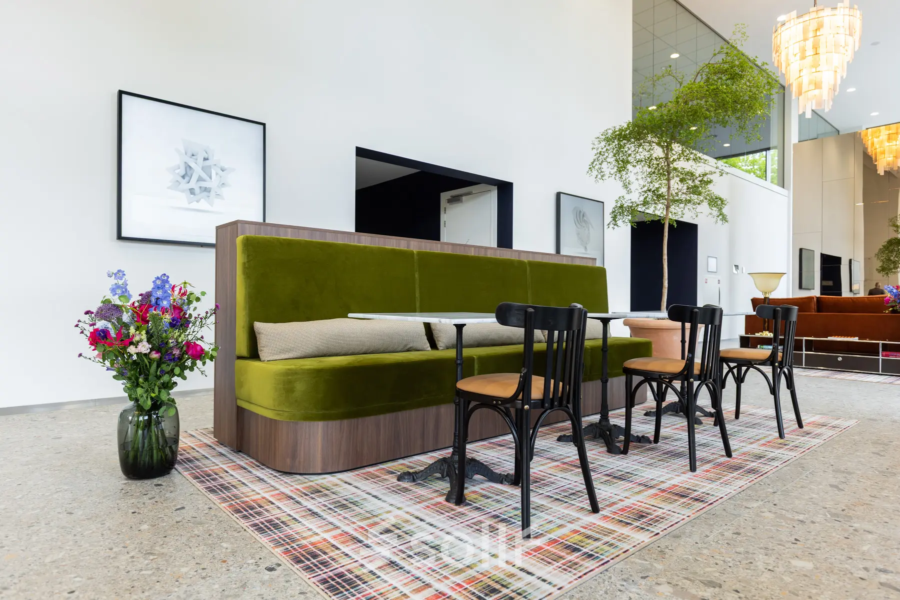 Modern gemeubileerde kantoorruimte in Amsterdam Amstel met groene bank, houten stoelen en een kleurrijk vloerkleed voor flexibel werken.