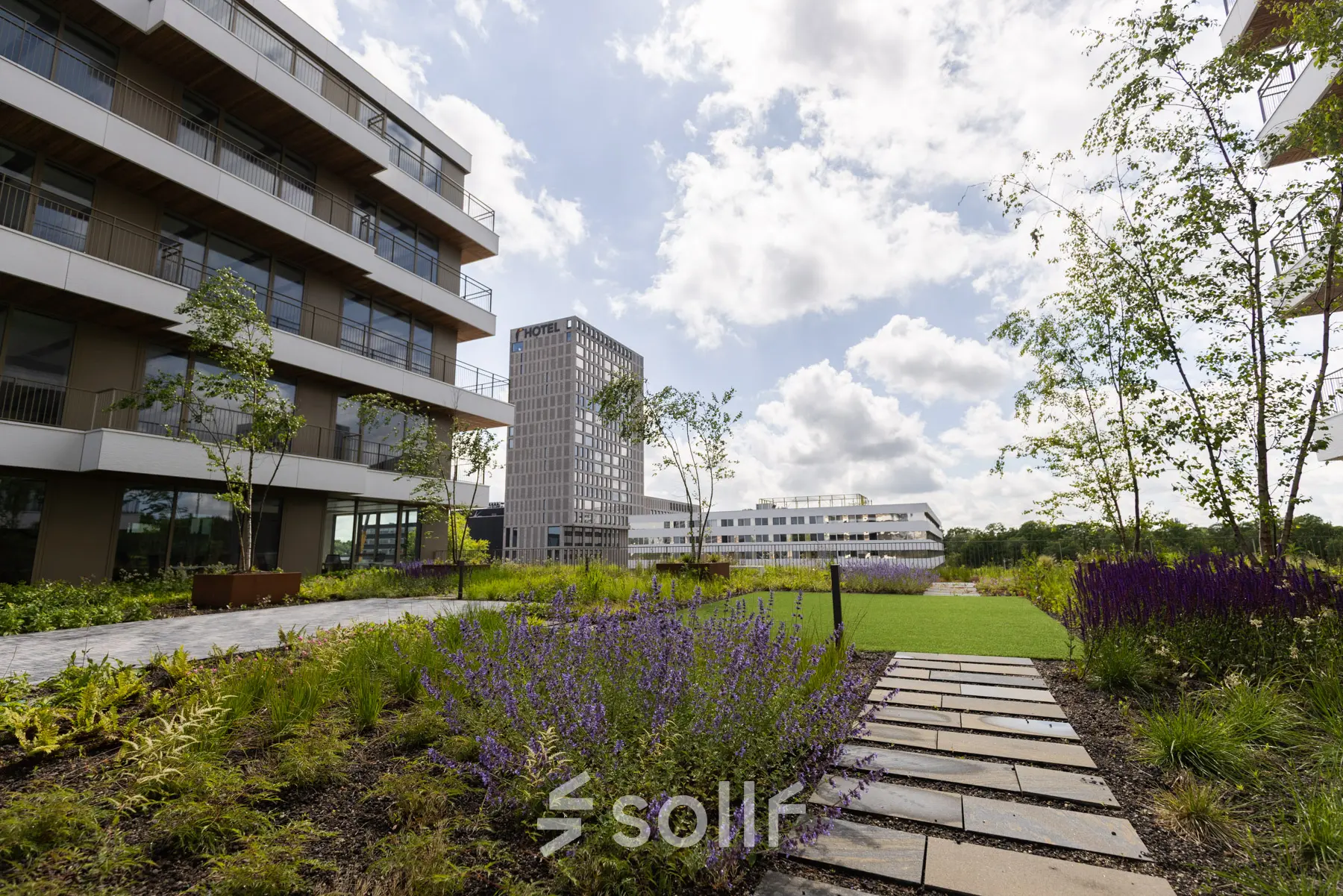 Exterieur van kantoorpand aan Willem Fenengastraat 16, Amsterdam Amstel, met moderne gebouwen en een groene tuin. Zonnige dag zonder mensen in beeld.