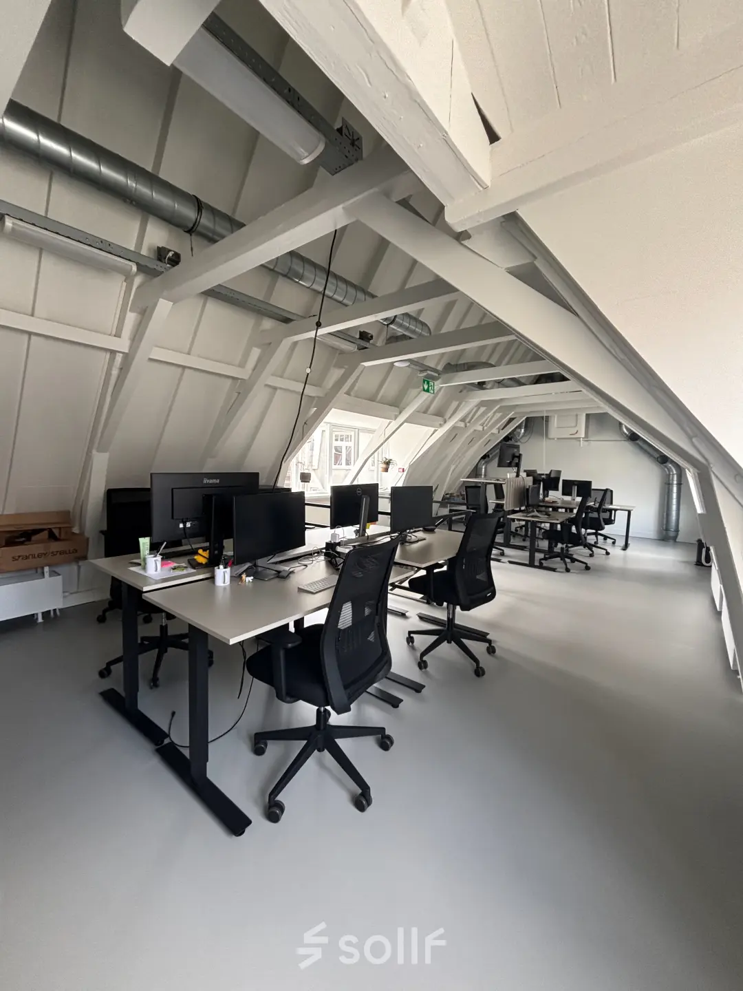 Moderne kantoorruimte te huur in Amsterdam Centrum, gelegen op Kloveniersburgwal 131K, ingericht met bureaus en computerschermen onder een karakteristiek schuin dak.