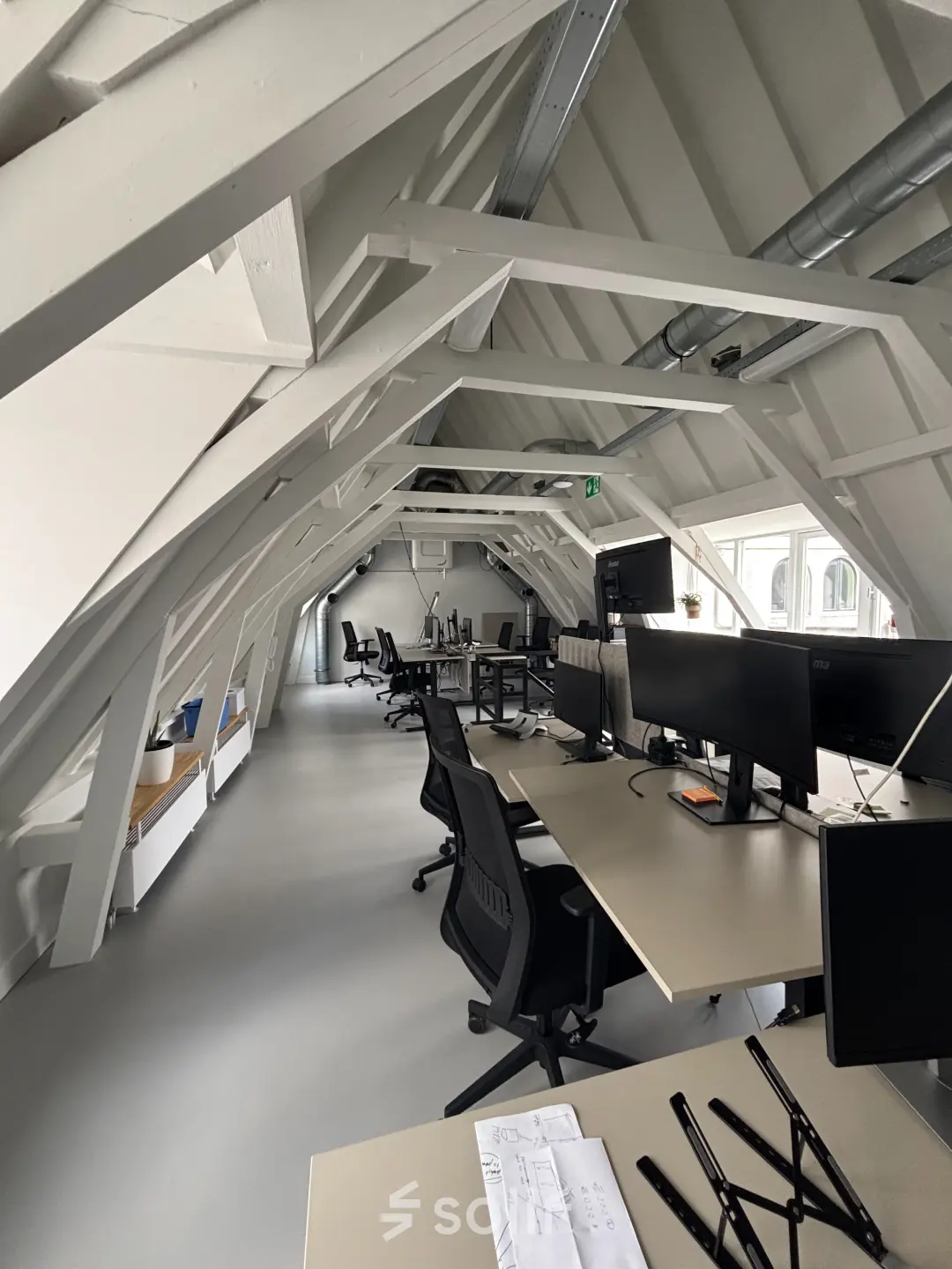 Moderne kantoorruimte huren aan de Kloveniersburgwal 131K in Amsterdam Centrum, met werkplekken onder karakteristieke balken, voorzien van bureaus en stoelen.