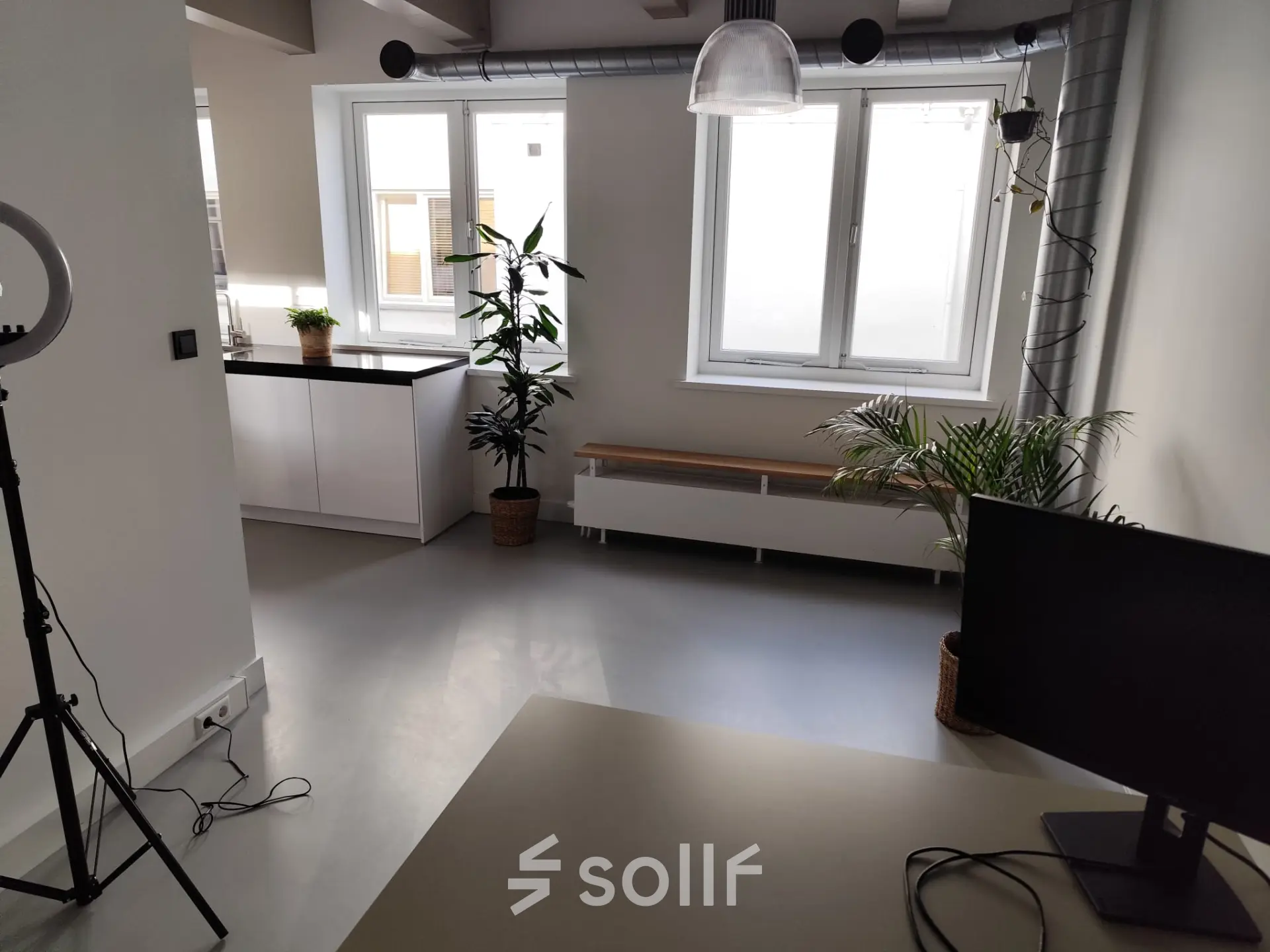 Lichte kantoorruimte in Amsterdam Centrum met moderne inrichting, geschikt om te huren. Het kantoorpand heeft grote ramen en is voorzien van planten en een bureau met scherm.