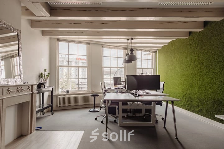 Modern kantoorpand in Amsterdam Centrum met bureaus en stoelen nabij een groene wand aan Prins Hendrikkade 14. Grote ramen zorgen voor veel lichtinval. Geschikt voor kantoorruimte huren.
