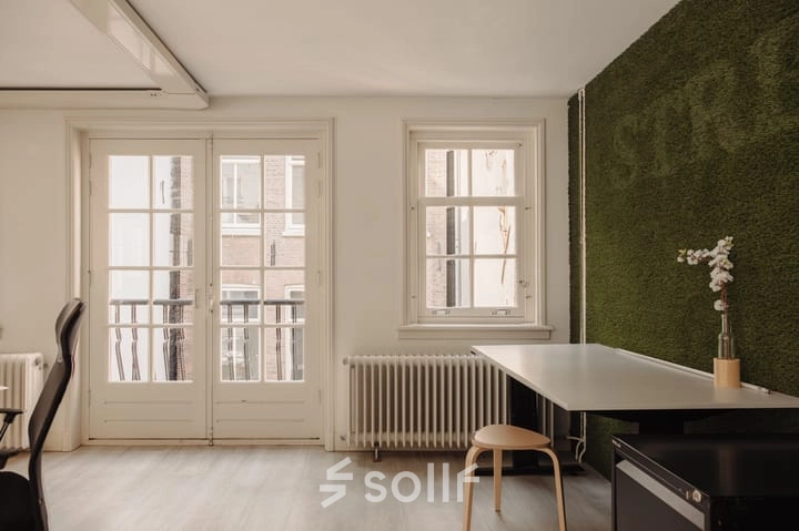 Kantoorruimte huren aan de Prins Hendrikkade 14 in Amsterdam Centrum, met uitzicht op aangrenzende gebouwen, voorzien van een tafel en stoelen, geschikt als werkruimte.