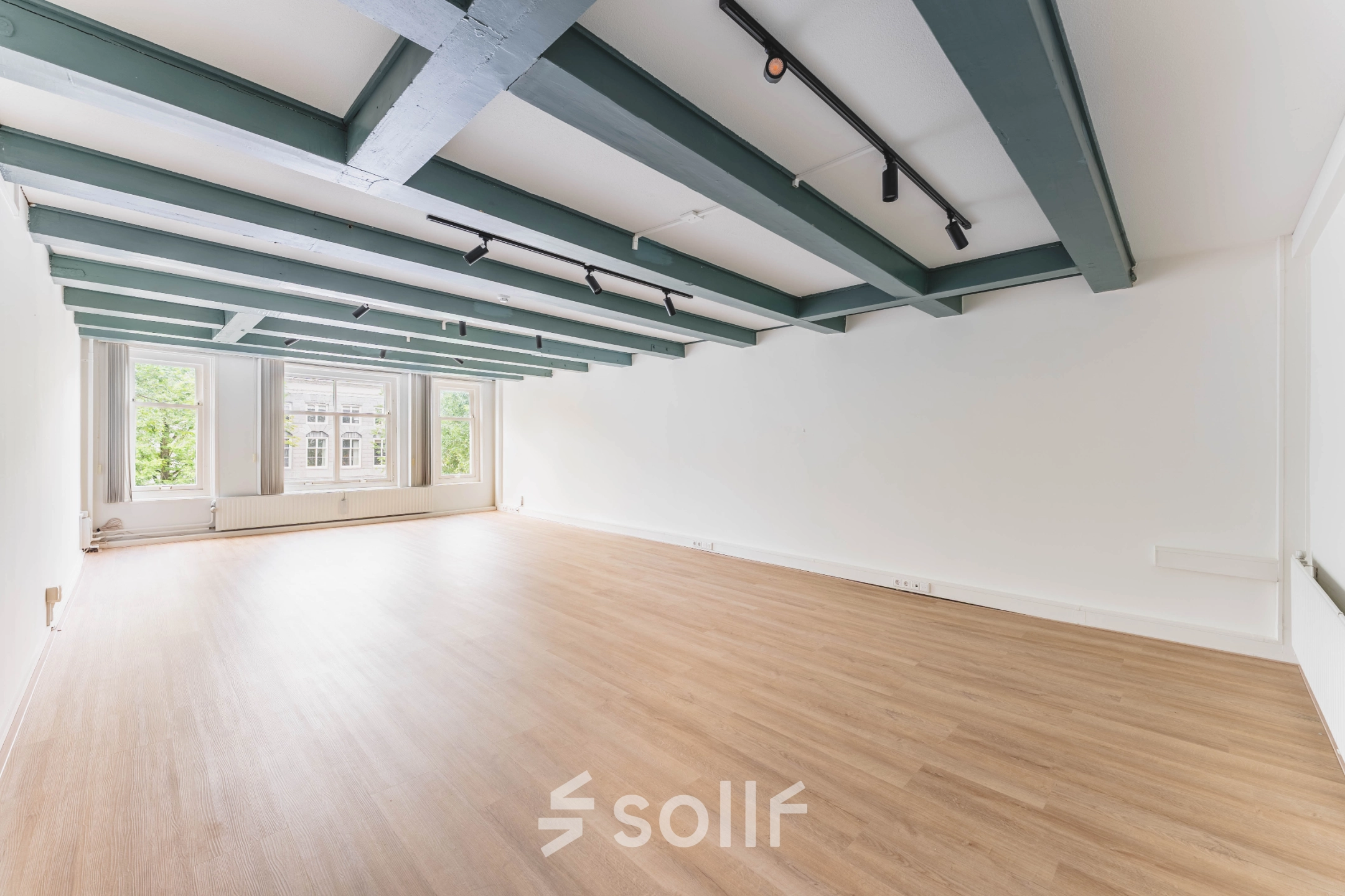 Leeg kantoorpand aan Herengracht 221, Amsterdam Grachtengordel, met houten vloer en balkenplafond, zicht op groene omgeving door grote ramen. Optimaal voor kantoorruimte huren.