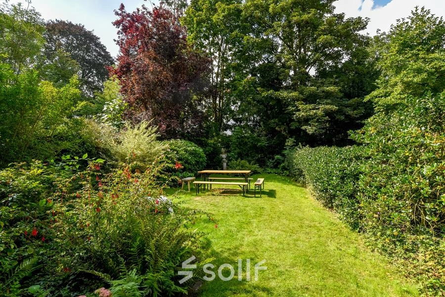 Groene buitenruimte van kantoor aan Herengracht 338, Amsterdam Grachtengordel, met grasveld en houten picknicktafel, omgeven door bloeiende struiken en bomen.