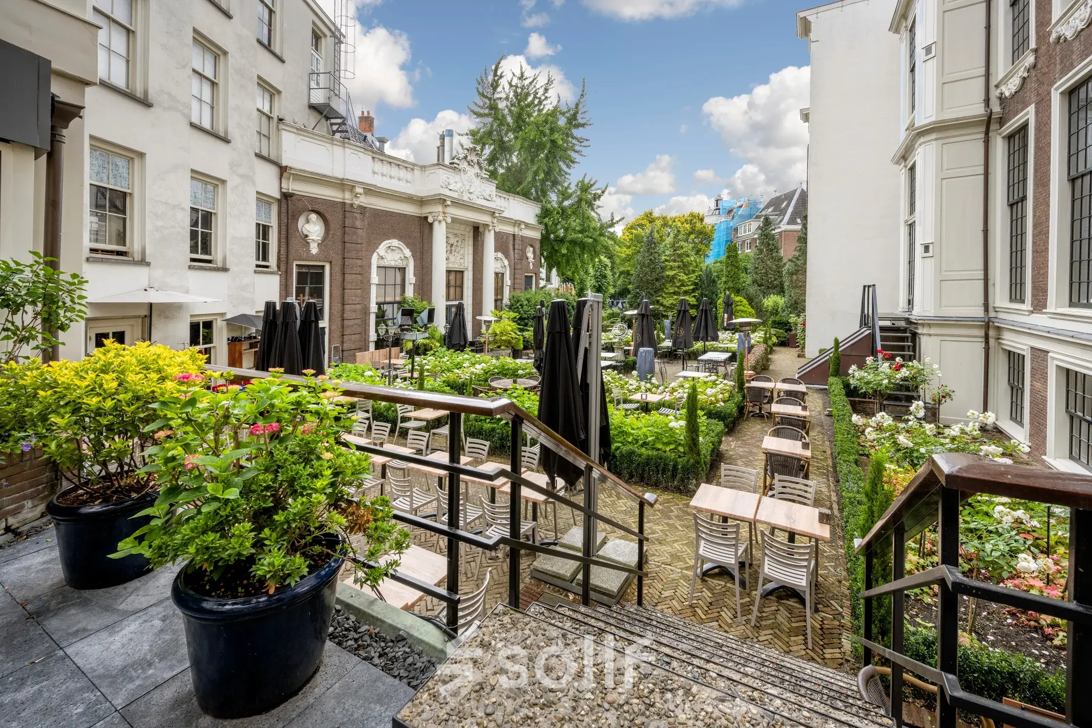 Buitenterras van het kantoorpand aan de Herengracht 459-469 in Amsterdam Grachtengordel, met tafels en stoelen te midden van groene planten en bloembedden.